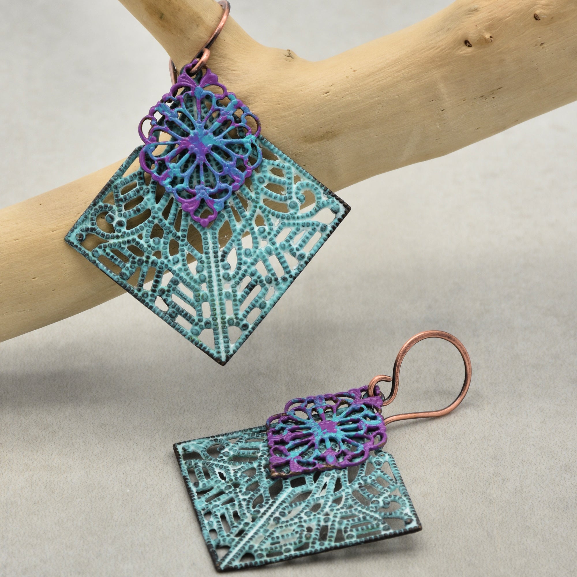 The image shows a pair of earrings. The jewelry pieces have hooks for wearing on pierced ears and feature an intricate, decorative design in blue and purple colors.