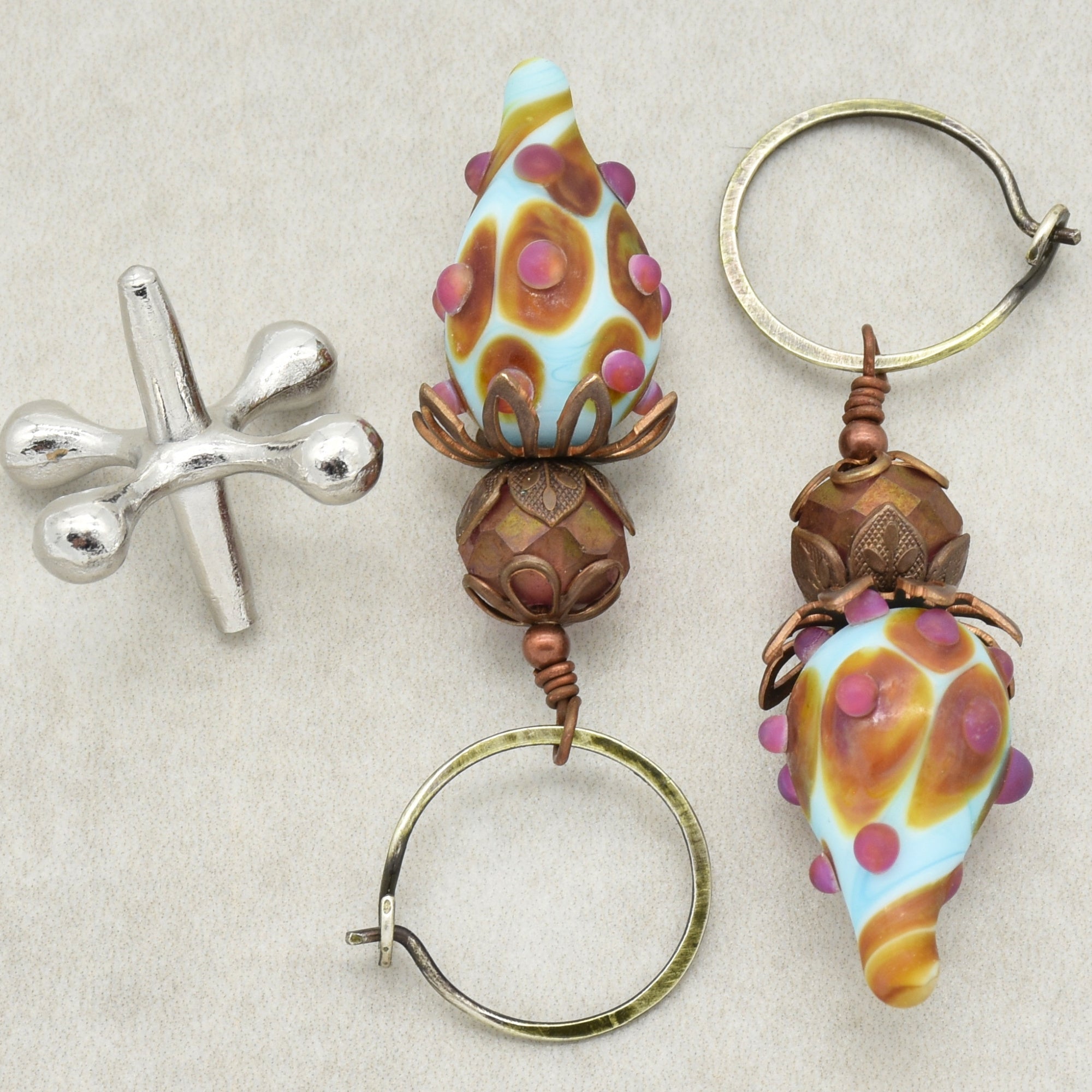 The image shows a pair of earrings. The jewelry pieces have hoop-style clasps and decorative elements that dangle from the hoops, which is characteristic of earrings.