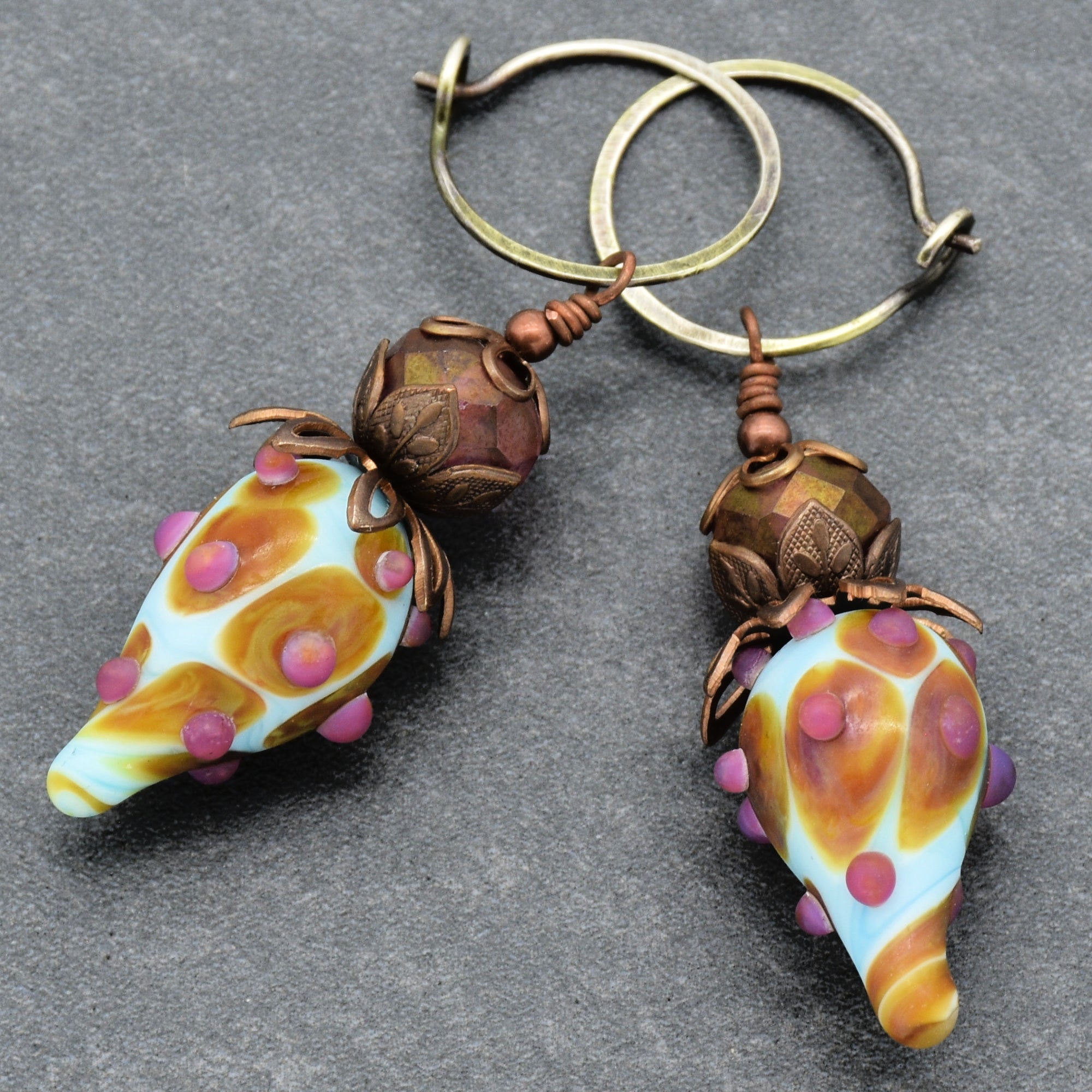 These are earrings. The image shows two pieces of jewelry with hoops designed to go through pierced ears, featuring decorative beads and elongated, colorful drops.