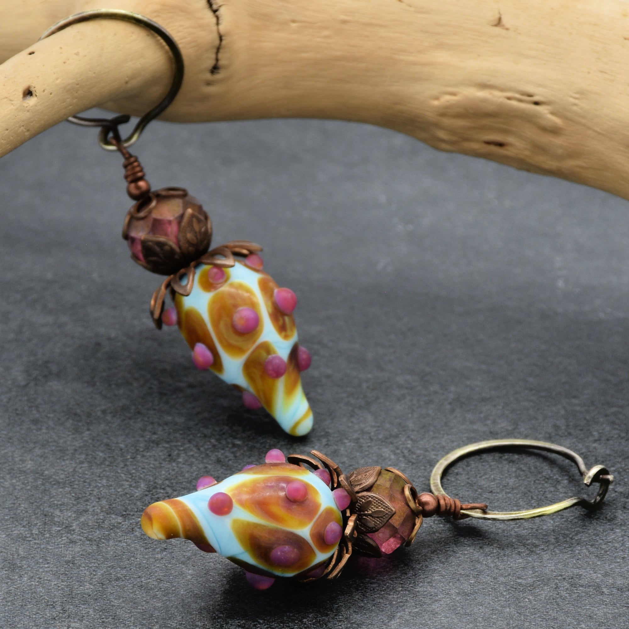 This image shows a pair of earrings. The jewelry pieces have metal hoops and decorative drops with intricate designs and colorful beads. They are not a necklace or bracelet.