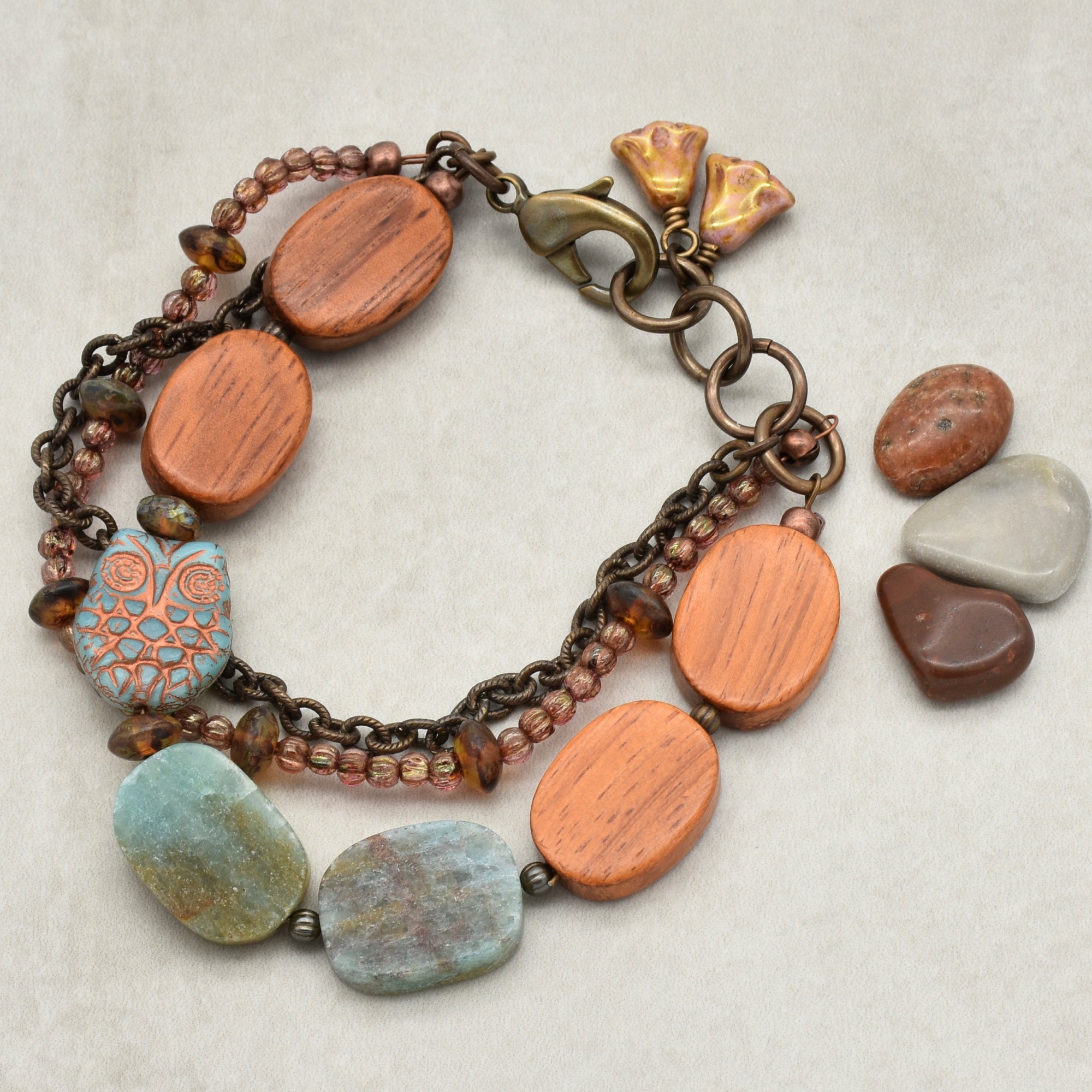 This image shows a bracelet. It is made of various beads including wooden, ceramic (with an owl design), and stone beads, connected with chains and a clasp for fastening around the wrist.