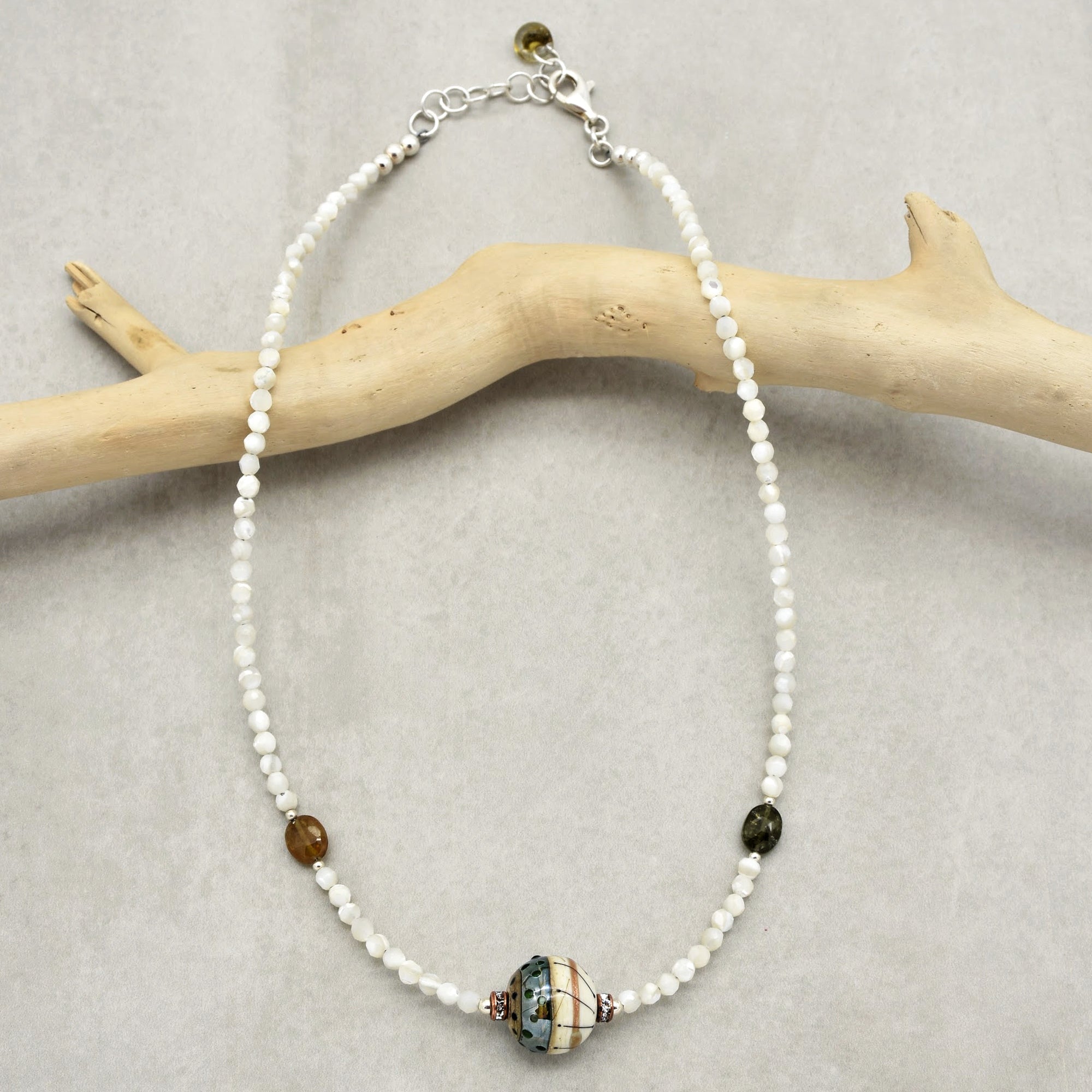 The image shows a necklace. It is composed of small white beads with a larger, multi-colored central bead and a couple of smaller beads on either side. The clasp at the top also indicates that it is designed to be worn around the neck.