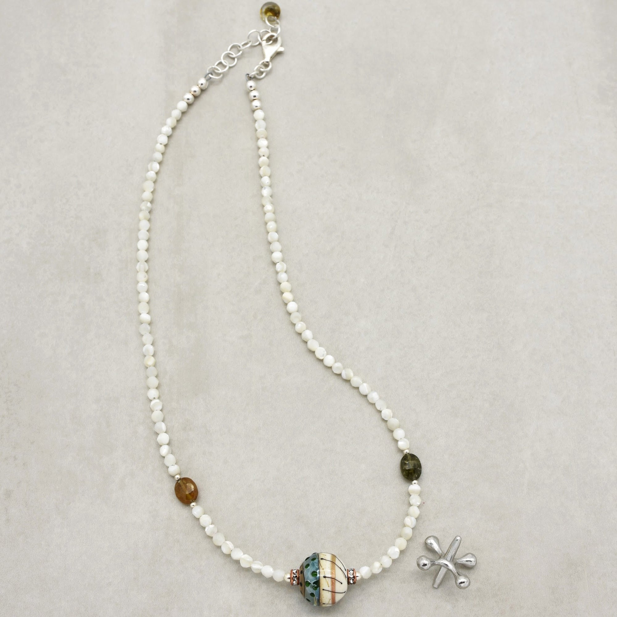 This image shows a necklace. It features a string of white beads with a few differently colored larger beads and a central, more decorative bead. The clasp and adjustable chain at the end are also characteristic features of a necklace.