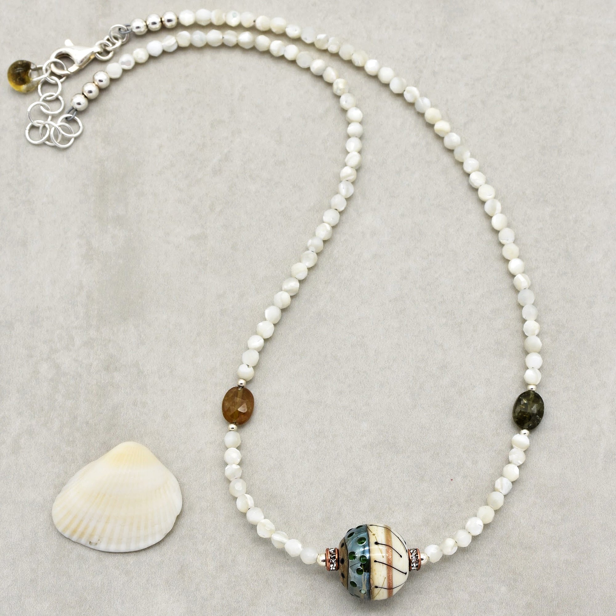 The image shows a necklace. It is made of small white beads with a larger decorative bead in the center and two distinct colored beads on either side. The clasp at the end also indicates that it is a necklace.