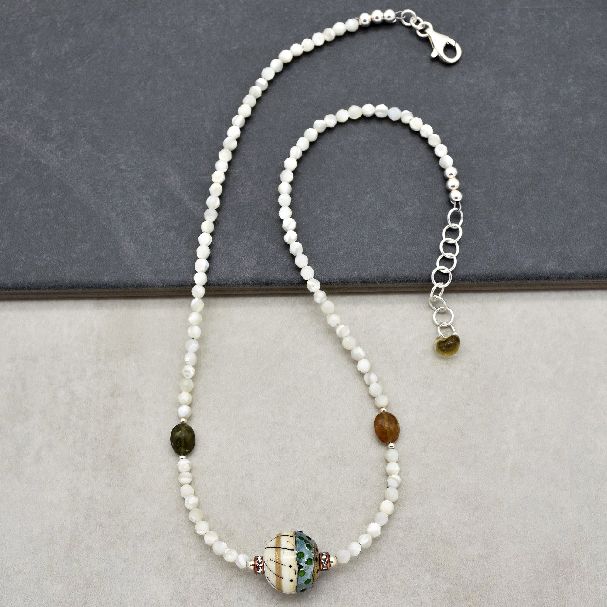 This image shows a necklace. It features small white beads strung together with a larger decorative bead in the center and a clasp at one end, which is typical for necklaces.