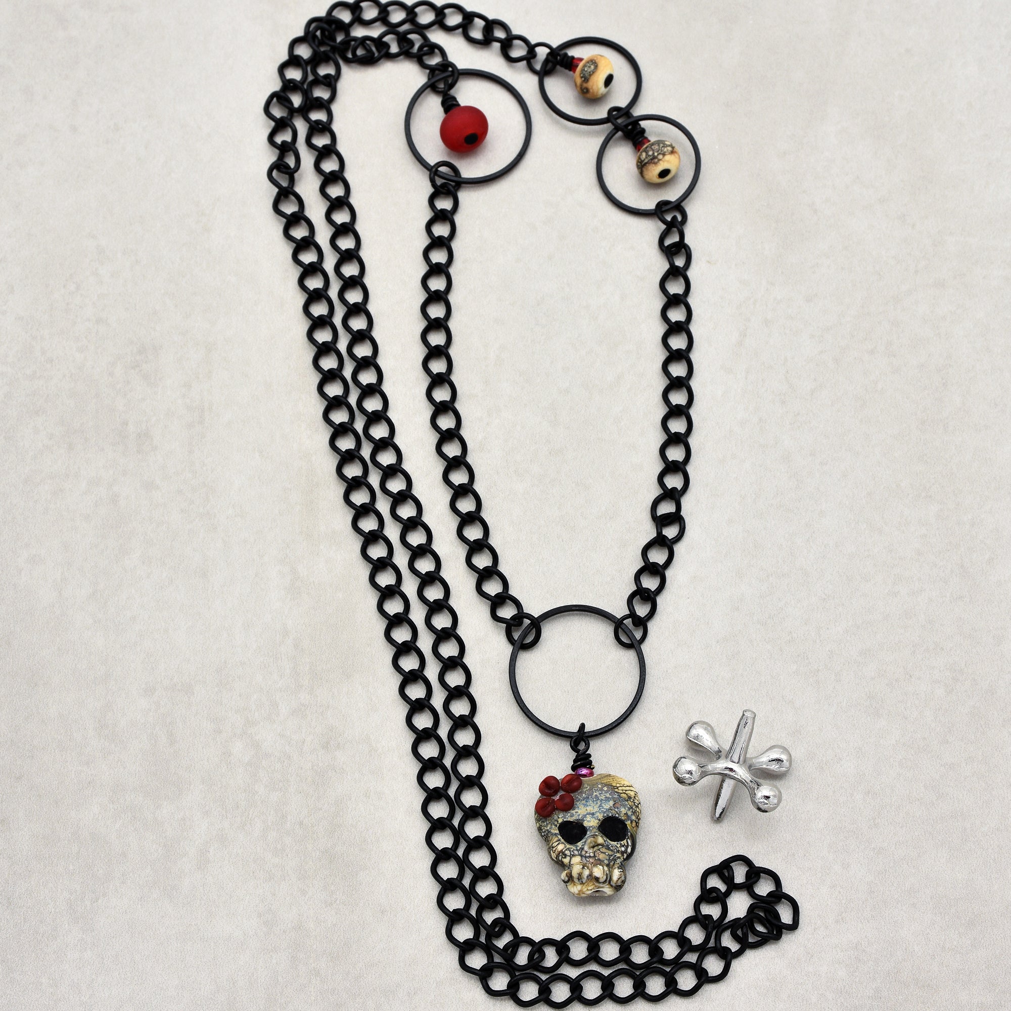This image shows a necklace. The jewelry features a black chain with a pendant in the shape of a skull and some additional decorative beads along the chain. It does not appear to be an earring or a bracelet.