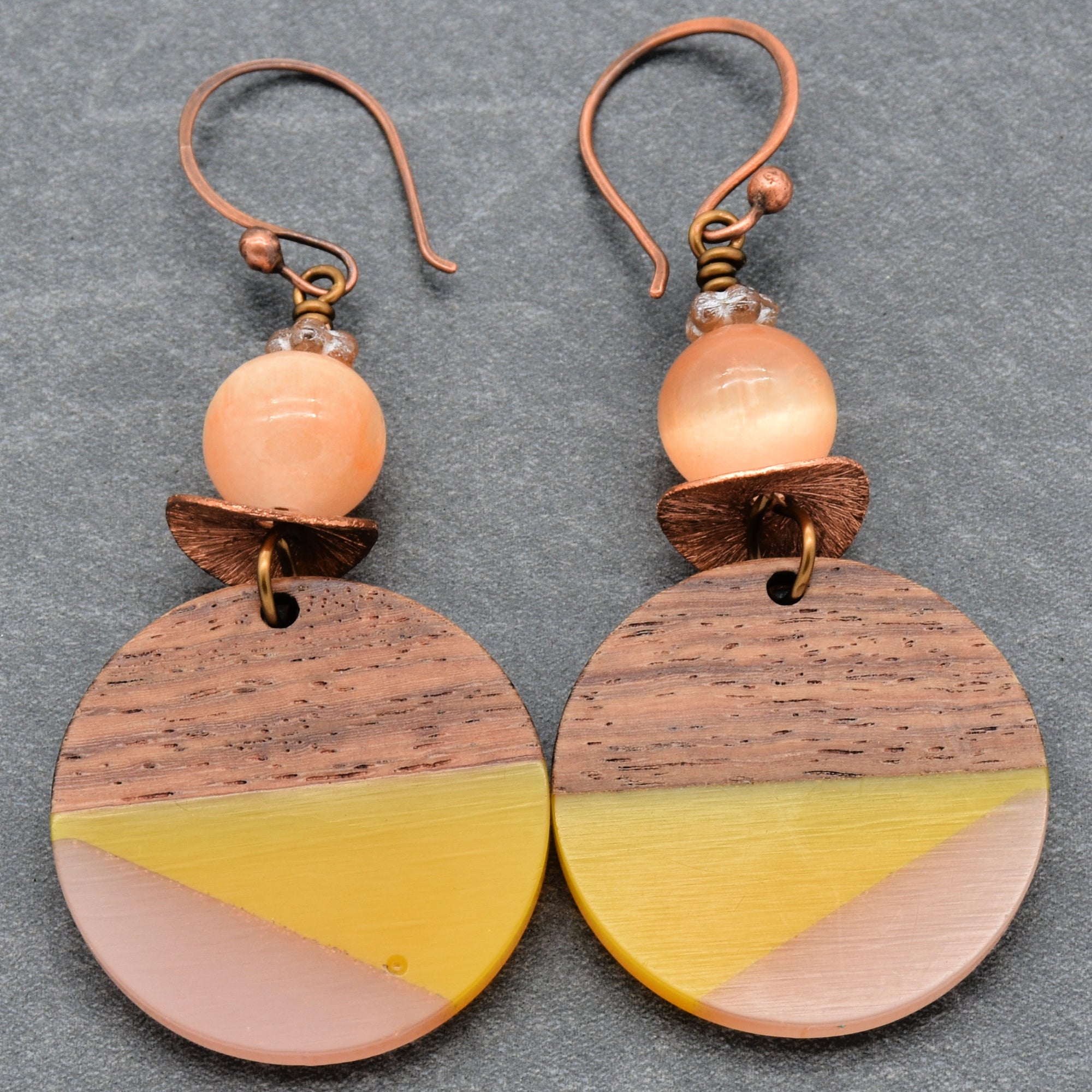 This image shows a pair of earrings. They have a hook for piercing the ear, round wood and colored elements, and a bead at the top.