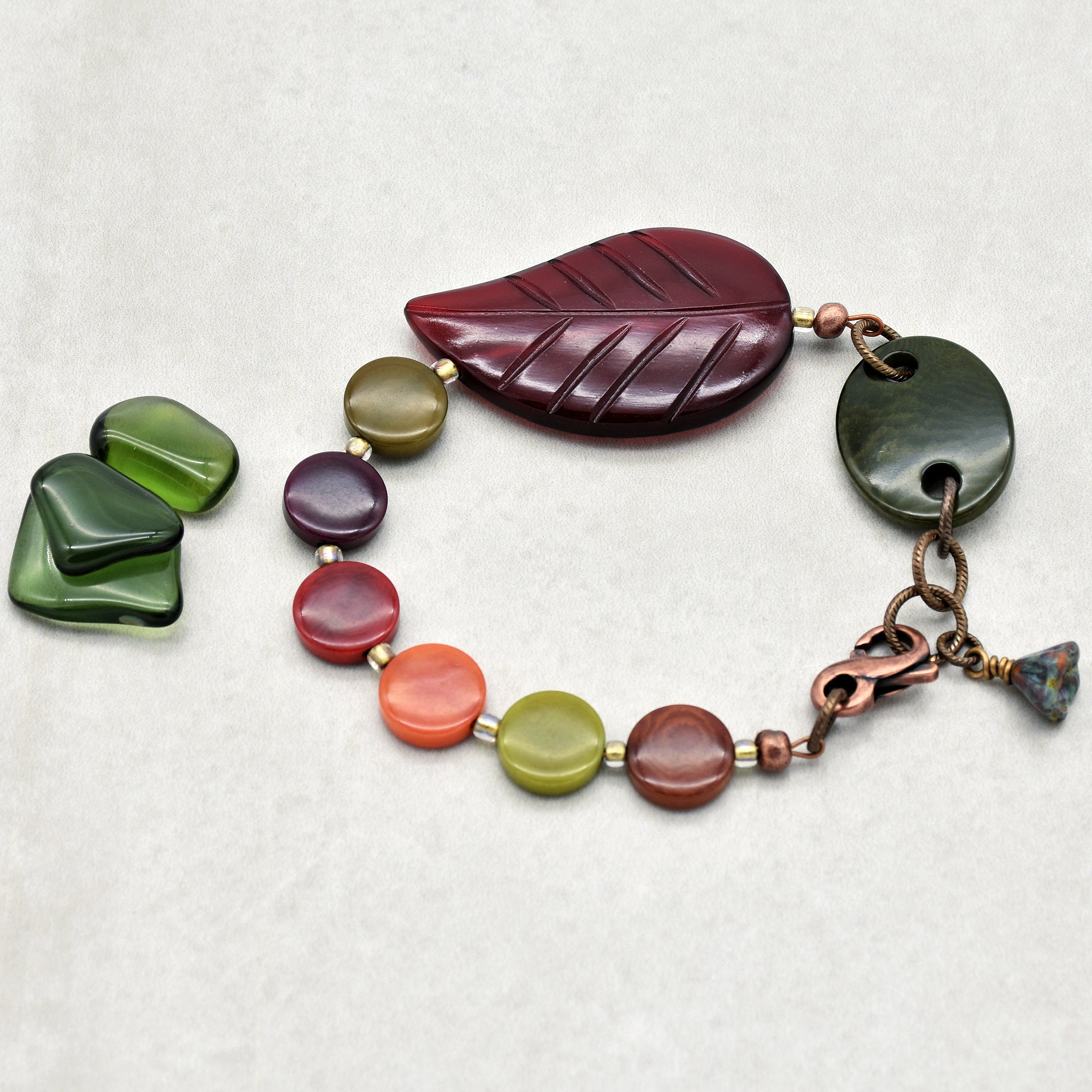 This image shows a bracelet. The size, bends into a circle, and the clasp are characteristic of bracelets. The design features colorful round beads and a large leaf-shaped bead as a focal point.