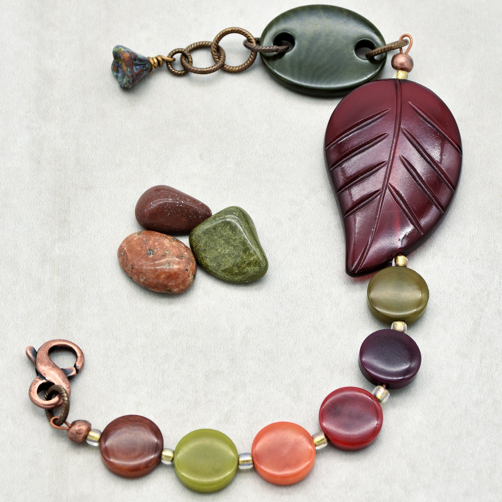 This image shows a piece of jewelry that looks like a bracelet. The size and the clasp indicate that it is designed to be worn around the wrist. The bracelet features a variety of beads with earthy tones and a decorative leaf-shaped piece.