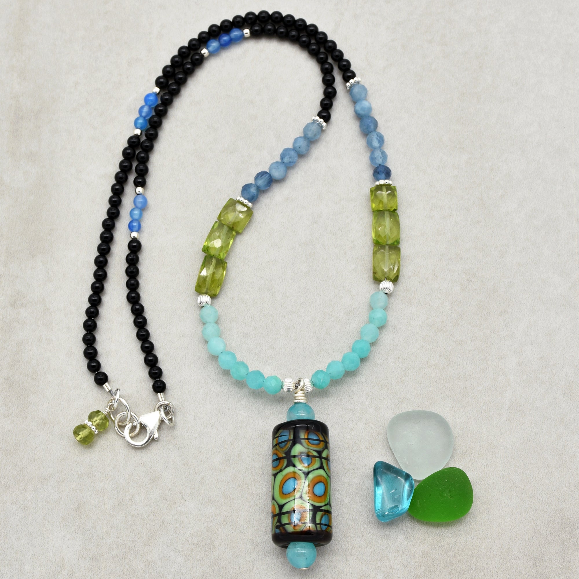 This image shows a necklace. The beads are arranged in a pattern typical for necklaces, and it has a pendant hanging in the center. Additionally, there is a clasp that would allow it to be worn around the neck.