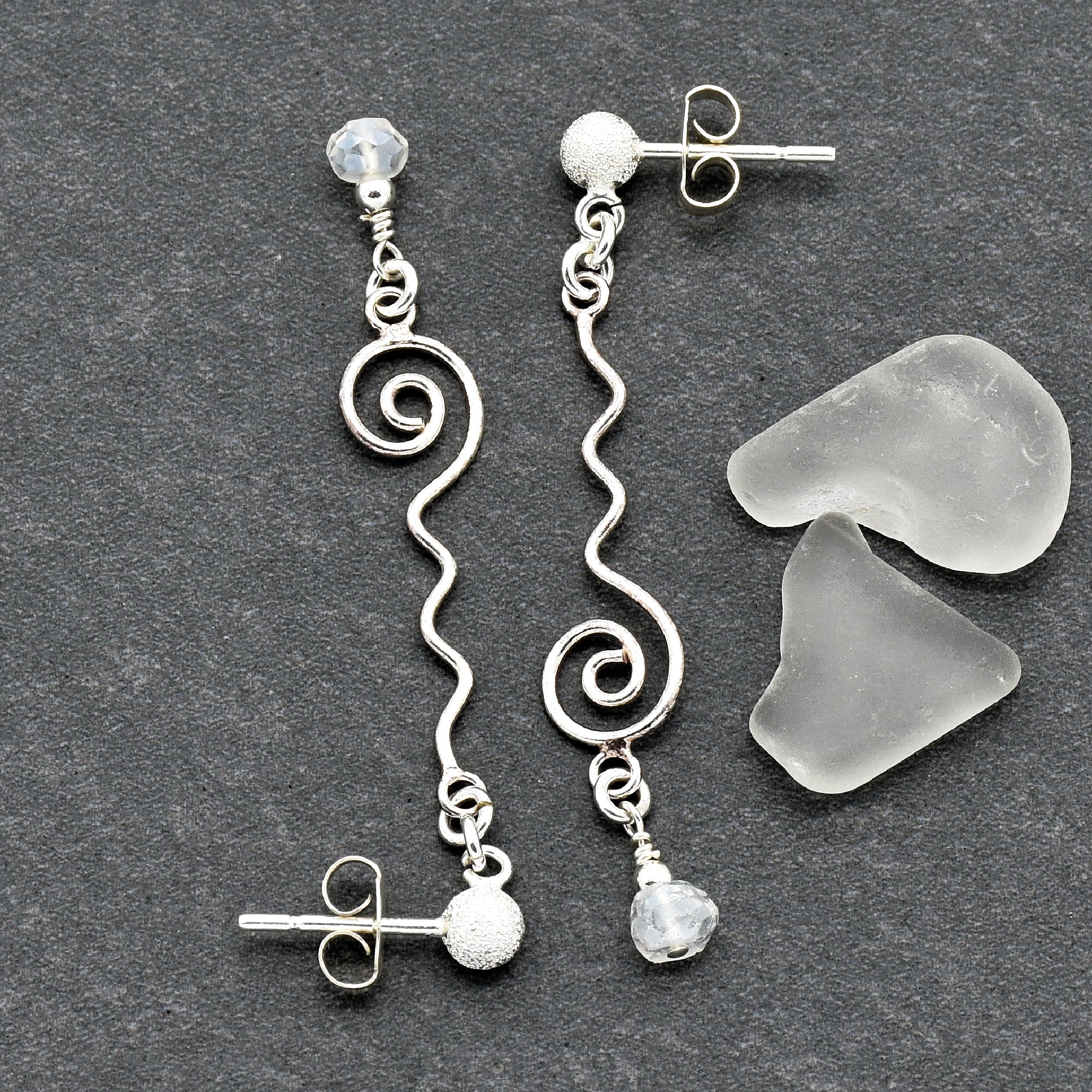 The jewelry in the image is a pair of earrings. They feature a spiral and wavy design in silver metal, with a stud and butterfly back for fastening.