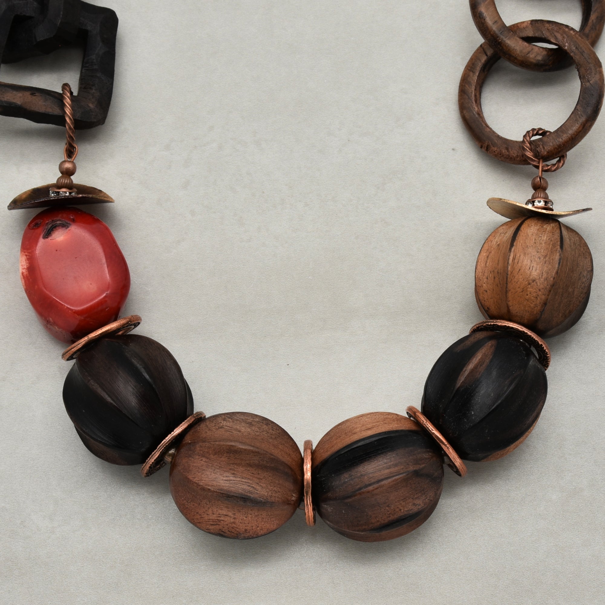 This image shows a necklace. The jewelry has large beads made of wood and a reddish stone, strung together with metal rings and twisted wire components. The design and length arrangement are typical for a necklace.