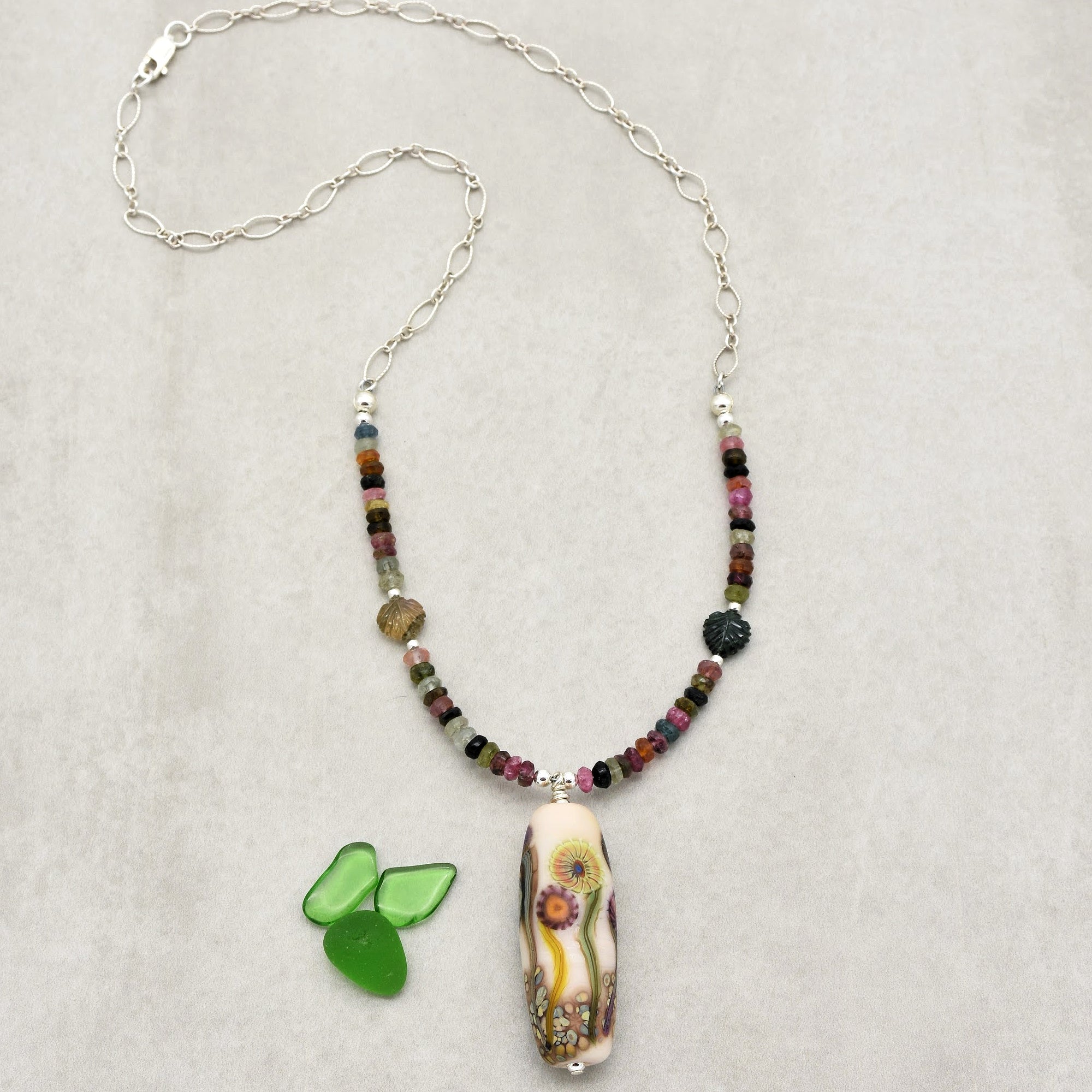 This image shows a necklace. It has a chain with various colorful beads and a decorative pendant hanging at the center.