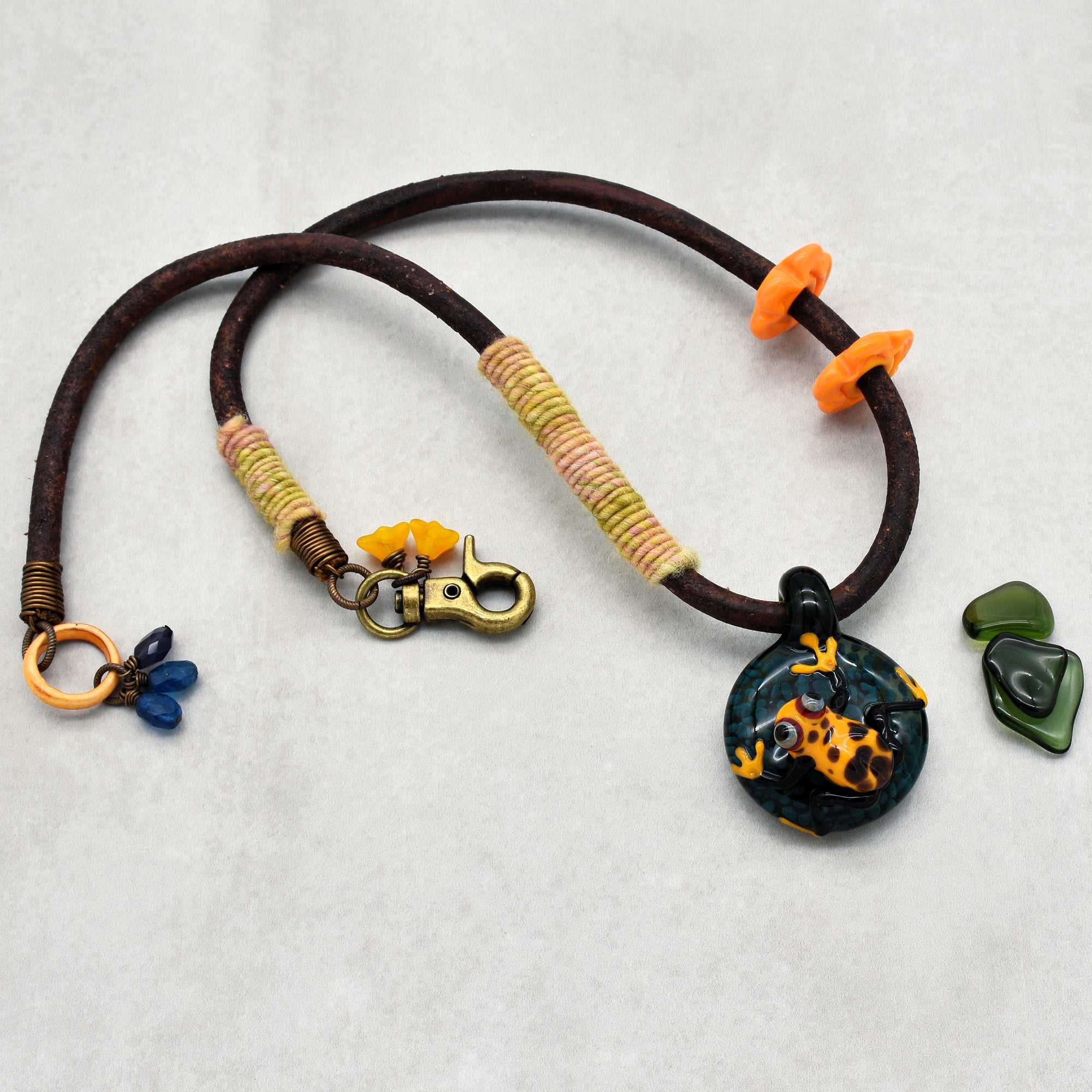 This image shows a necklace. The item has a pendant featuring a colorful frog, attached to a cord with a clasp, which is characteristic of necklaces.