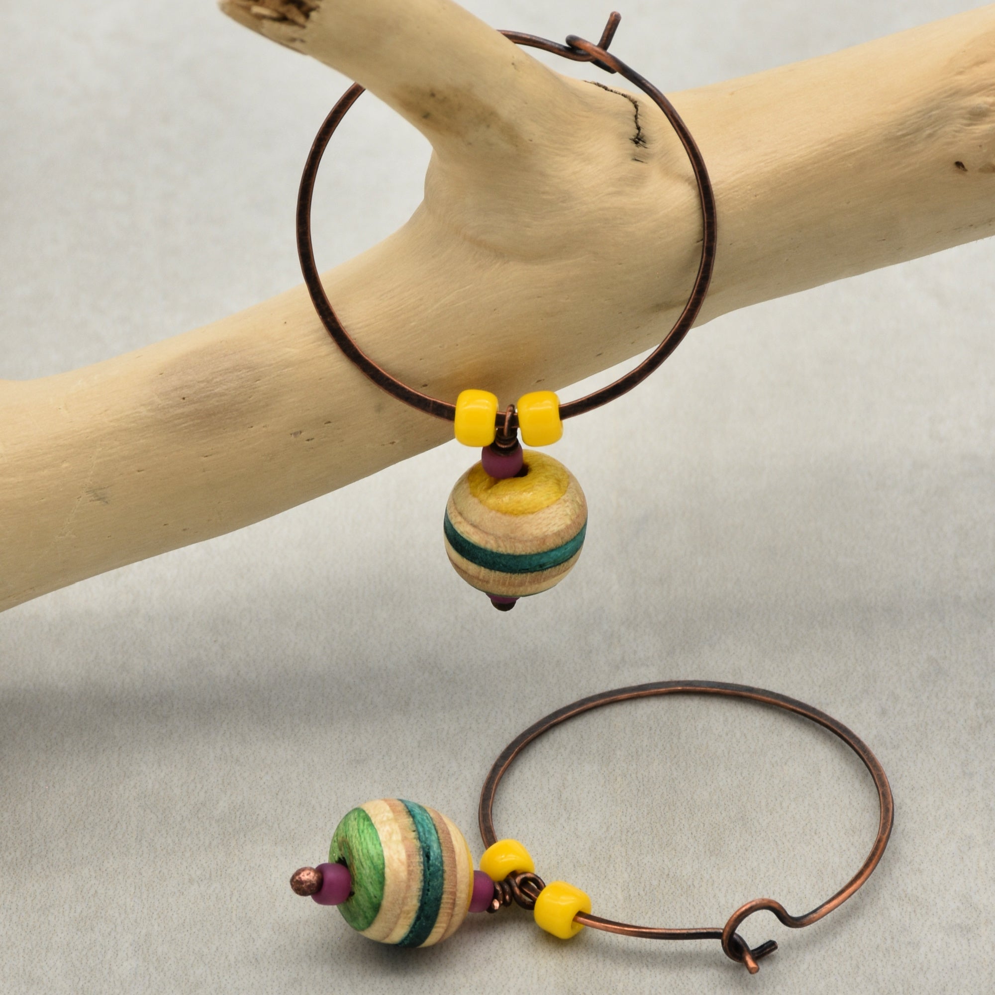 The image shows a pair of earrings. They are hoop-style earrings with colorful beads, including a striped round bead and two small yellow beads on each hoop.