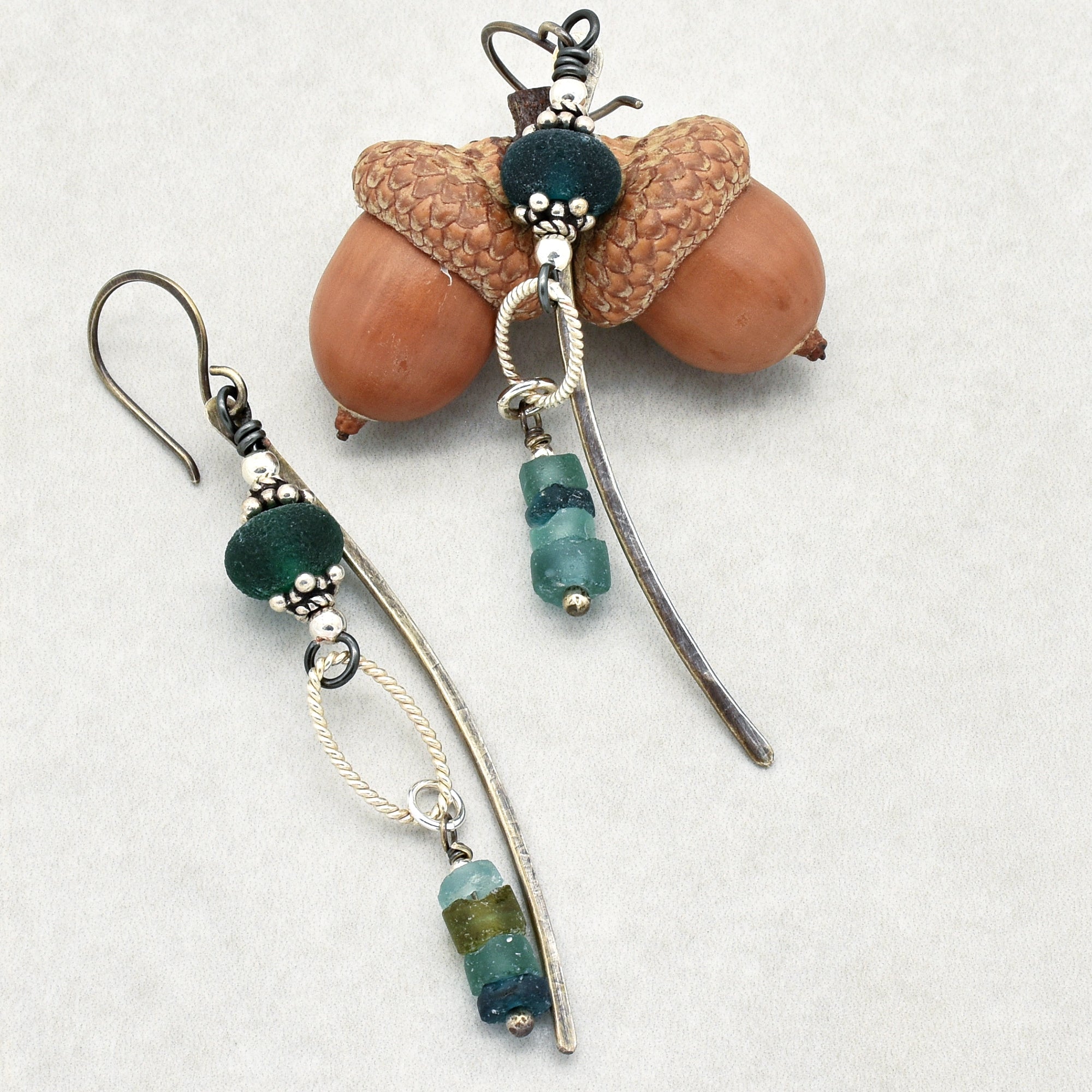 The image shows a pair of earrings. They have a hook at the top for piercing through the ear, and they include decorative elements made of metal and beads with a curved design.