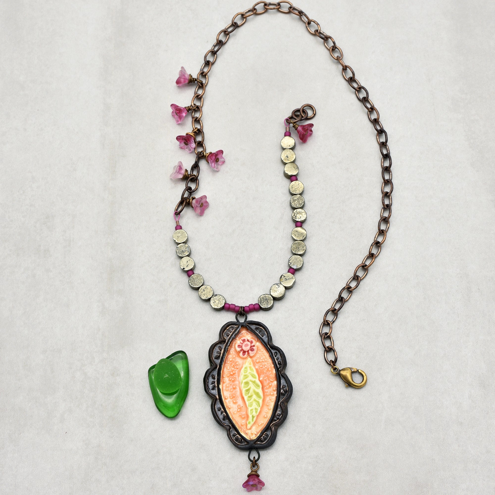 This image shows a necklace. The jewelry piece has a chain with a clasp, beads, small pink flower-shaped charms, and a central pendant with a floral design. The length and shape indicate it is meant to be worn around the neck.