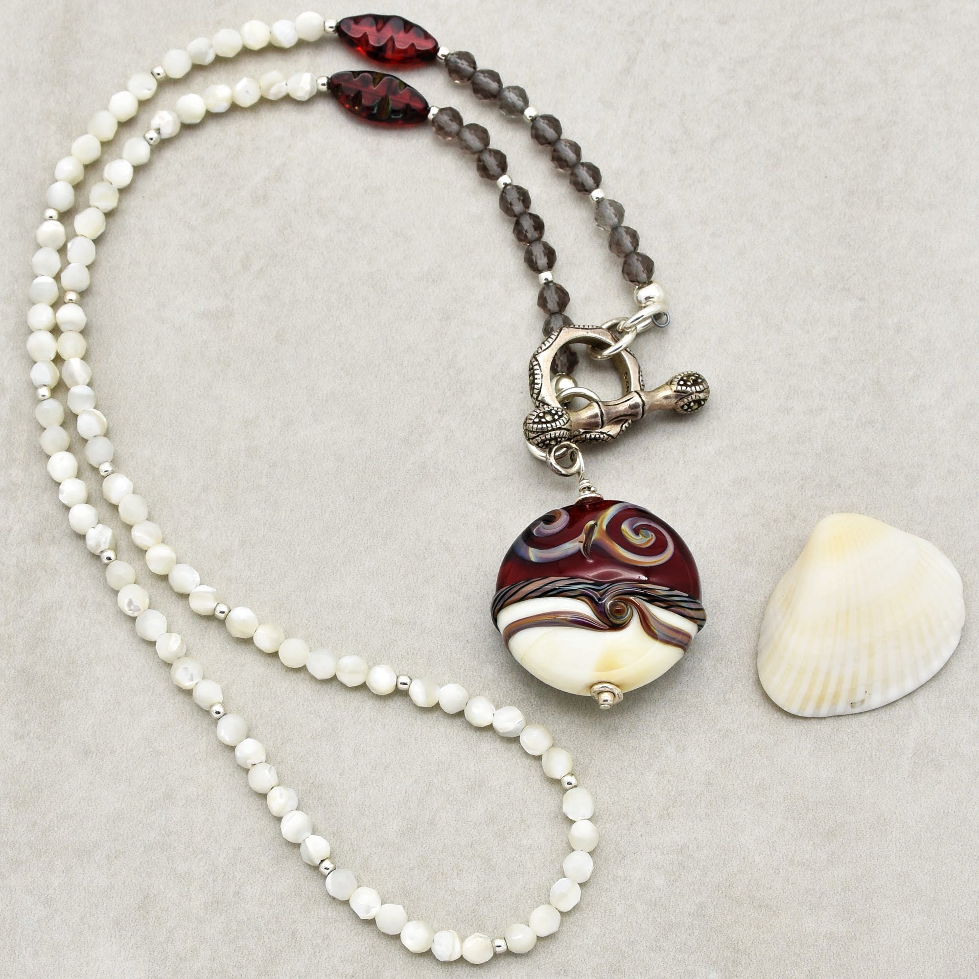 This image shows a necklace. The jewelry has a string of beads and a large, decorative pendant attached to a clasp. The length and design suggest it is a necklace rather than an earring or a bracelet.