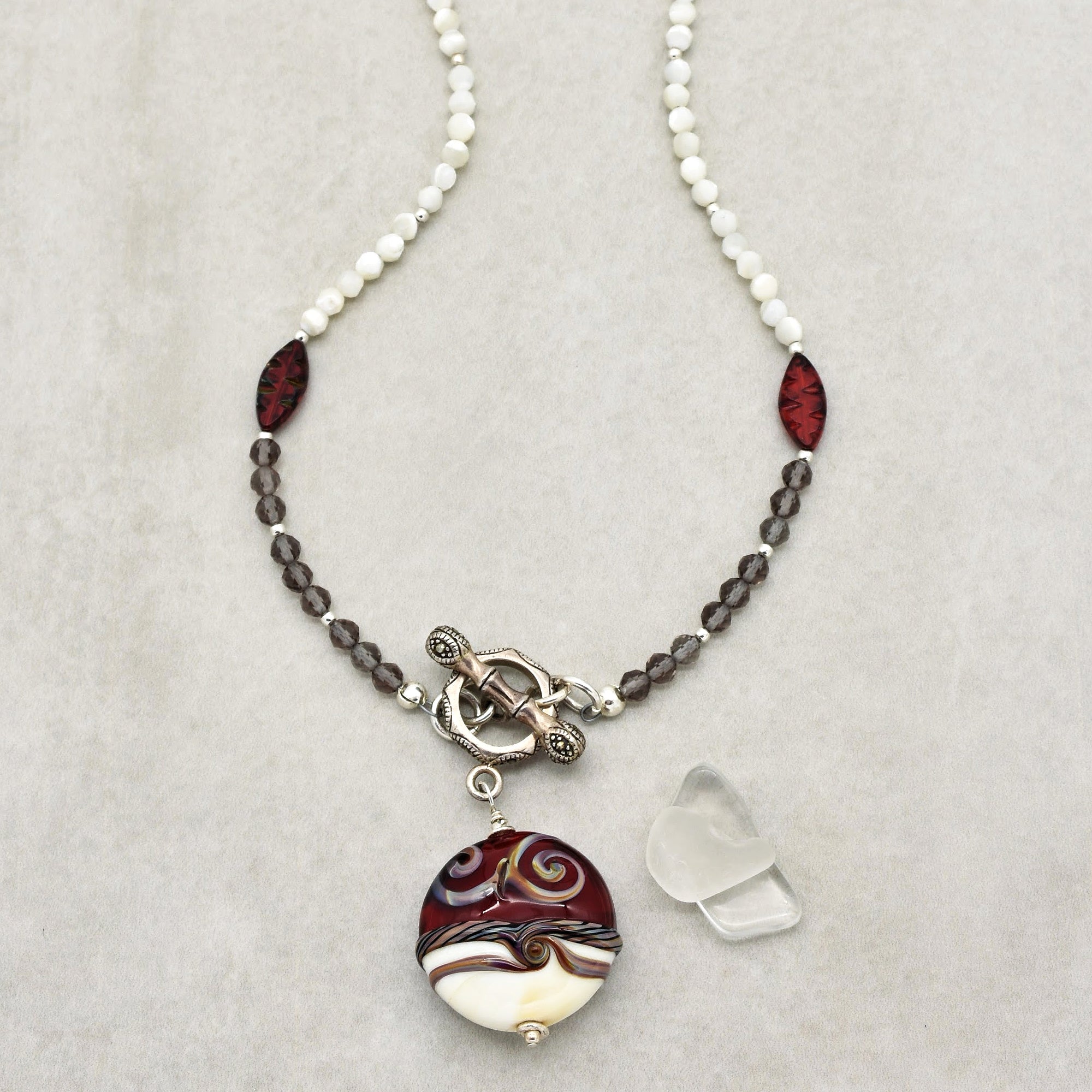 This image shows a necklace. It features beads in multiple colors and shapes, with a prominent round pendant hanging from the center. The necklace also has a decorative clasp.
