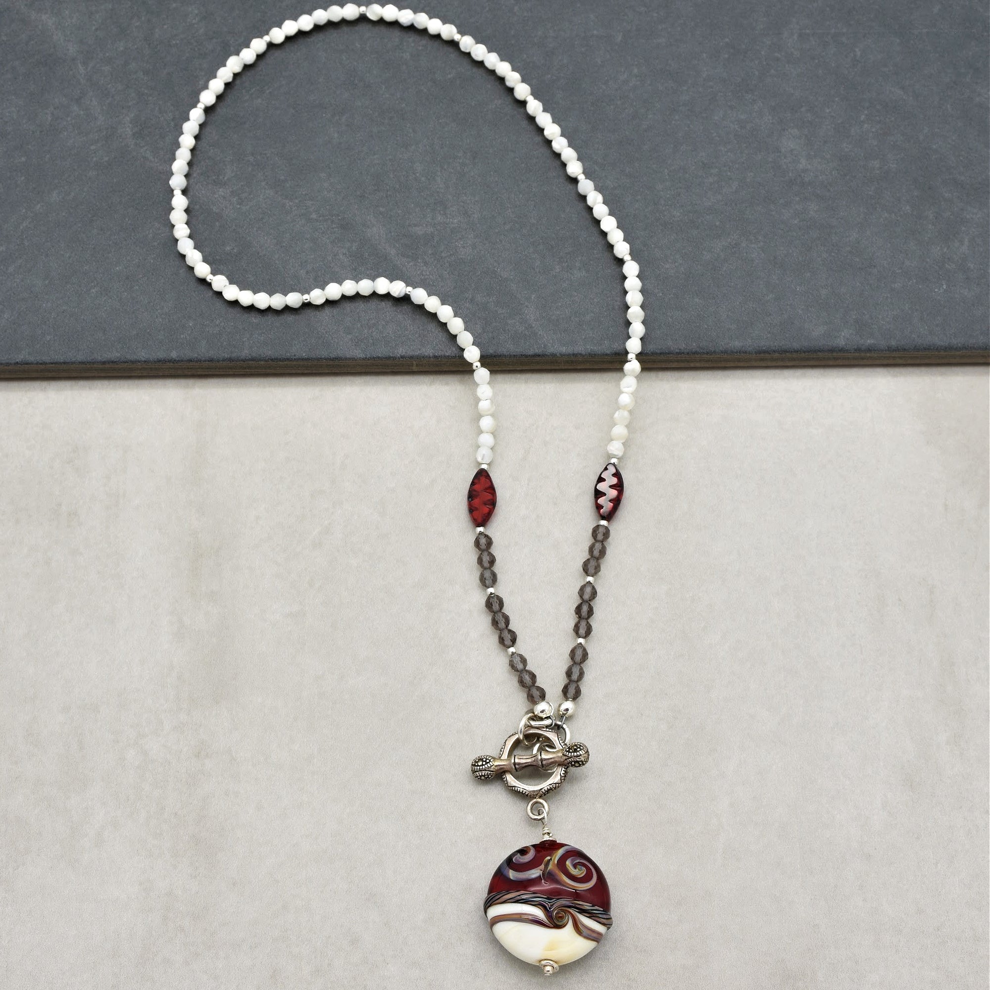 This image shows a necklace. It is characterized by a string of beads with a pendant hanging from the bottom, which is typical of necklaces. It is not a bracelet or earring.