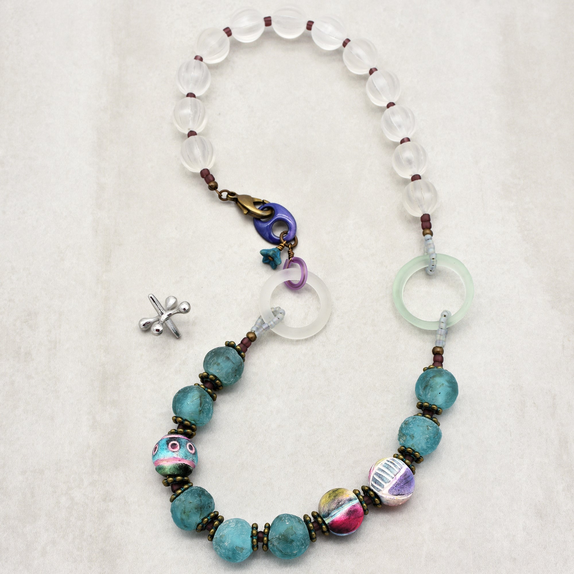 This image depicts a necklace. The jewelry is composed of a variety of beads, including translucent and colorful decorative beads, strung together in a pattern, and it has a clasp at one end for fastening around the neck. The length and shape of the item also indicate that it is a necklace rather than an earring or bracelet.