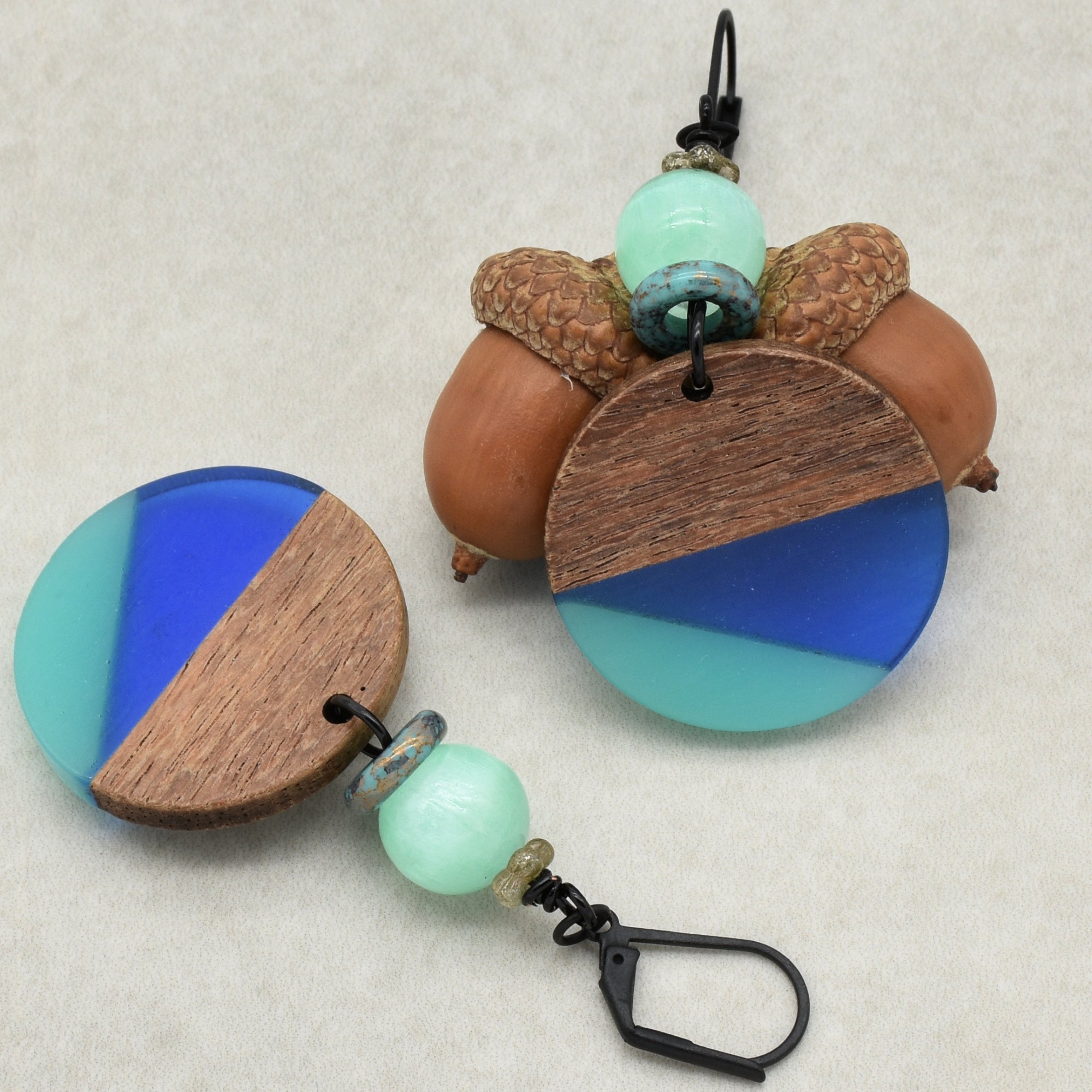 This image shows a pair of earrings. The jewelry pieces have a circular design with a combination of wood and blue colors, and they include beads and black hooks, which are typical components of earrings.