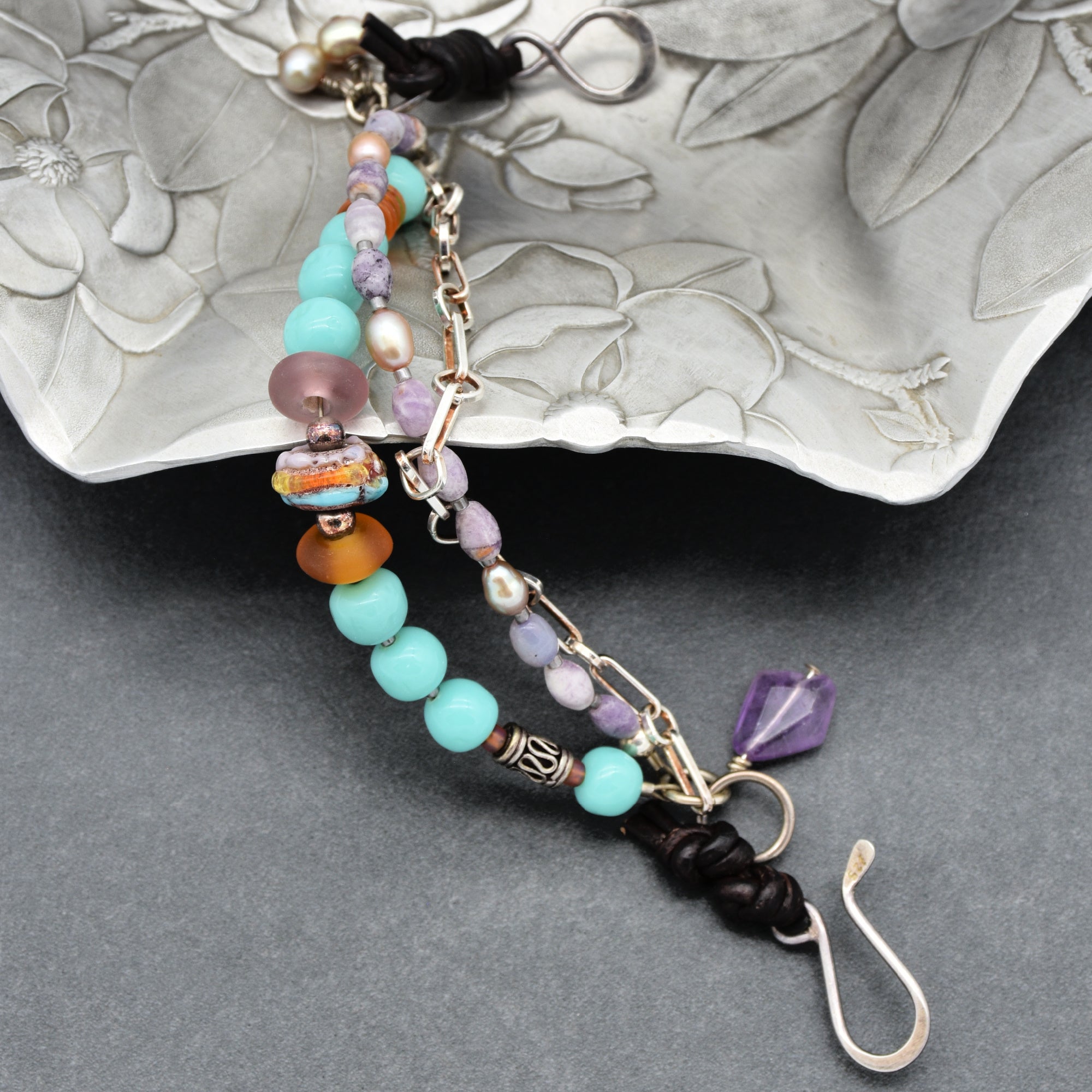 This image shows a bracelet. It has multiple strands with beads in various colors such as turquoise, purple, orange, and pearl-like beads, along with a metal chain and a hook clasp. The size and clasp type suggest it is designed to be worn around the wrist.