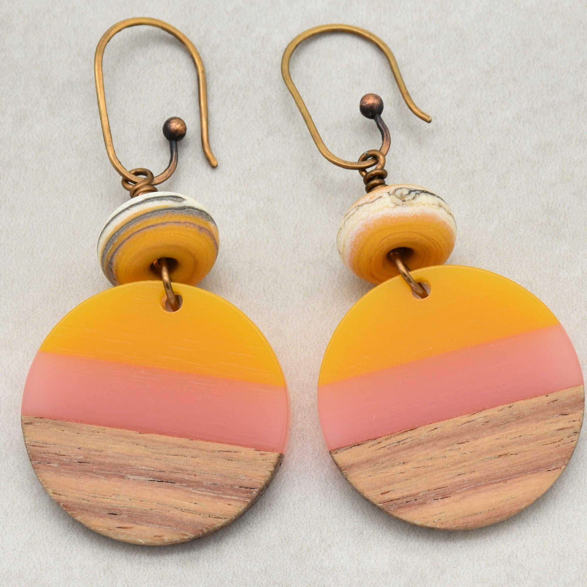 The image shows a pair of earrings. They have hooks for piercing, which is characteristic of earrings. The design includes round wooden and colored components.