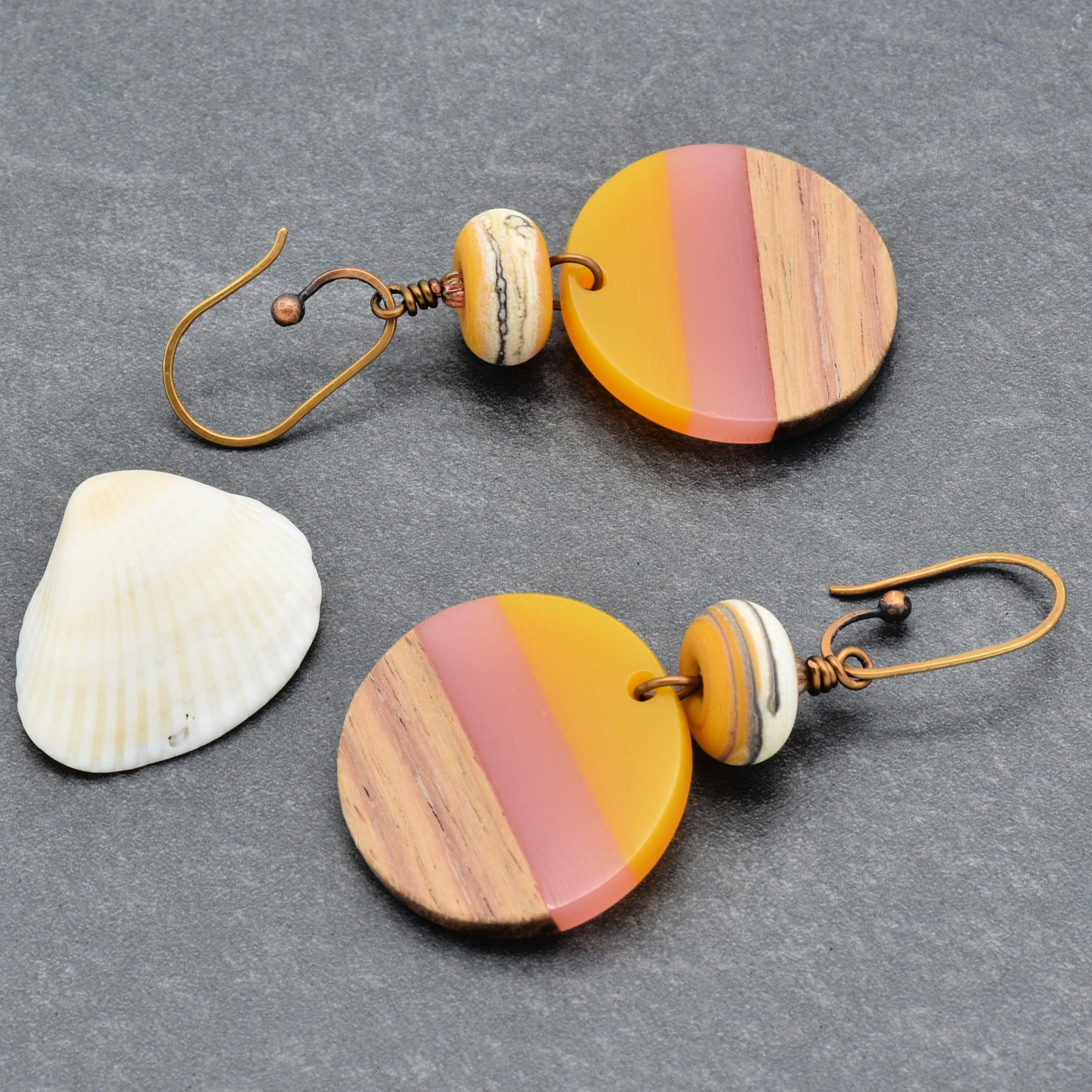 The image shows a pair of earrings. They have hooks for pierced ears and feature round, multicolored pendants with striped patterns made of wood and colored material.