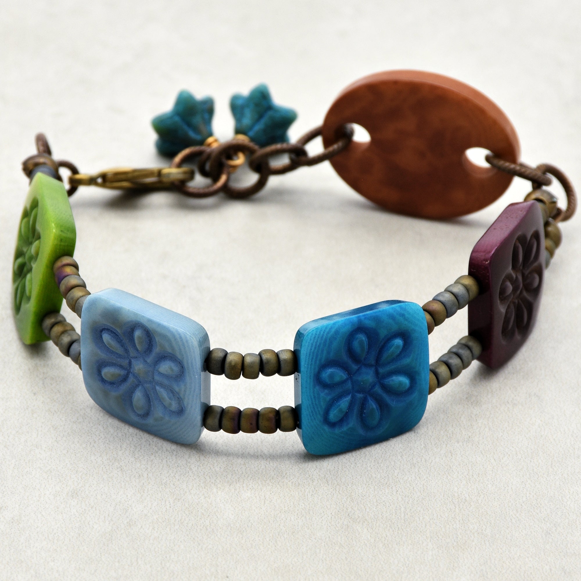 This image shows a bracelet. It features colorful rectangular beads with floral patterns, arranged on two strands of small round beads, and has a clasp for fastening.