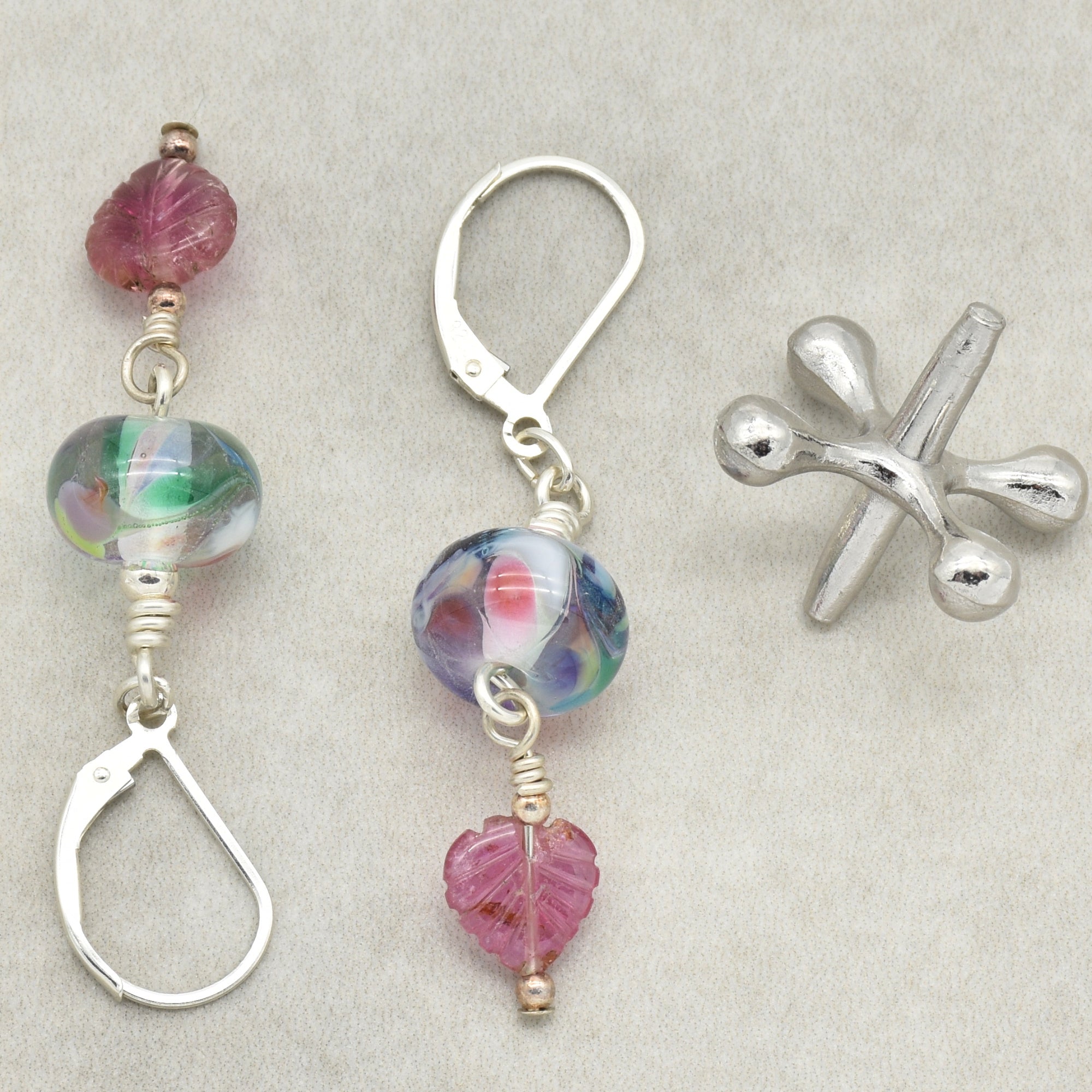 This image shows a pair of earrings. The earrings feature colorful glass beads and metal hooks for wearing. The metal object on the right is a jack, which is not jewelry.