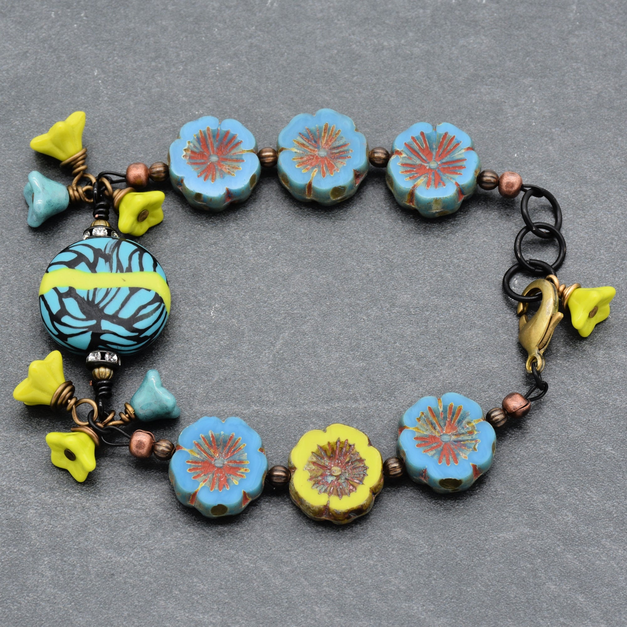 This image shows a bracelet. The jewelry has flower-shaped beads in blue and yellow, as well as a round decorative bead with a blue and yellow pattern. The bracelet also features a clasp for fastening.