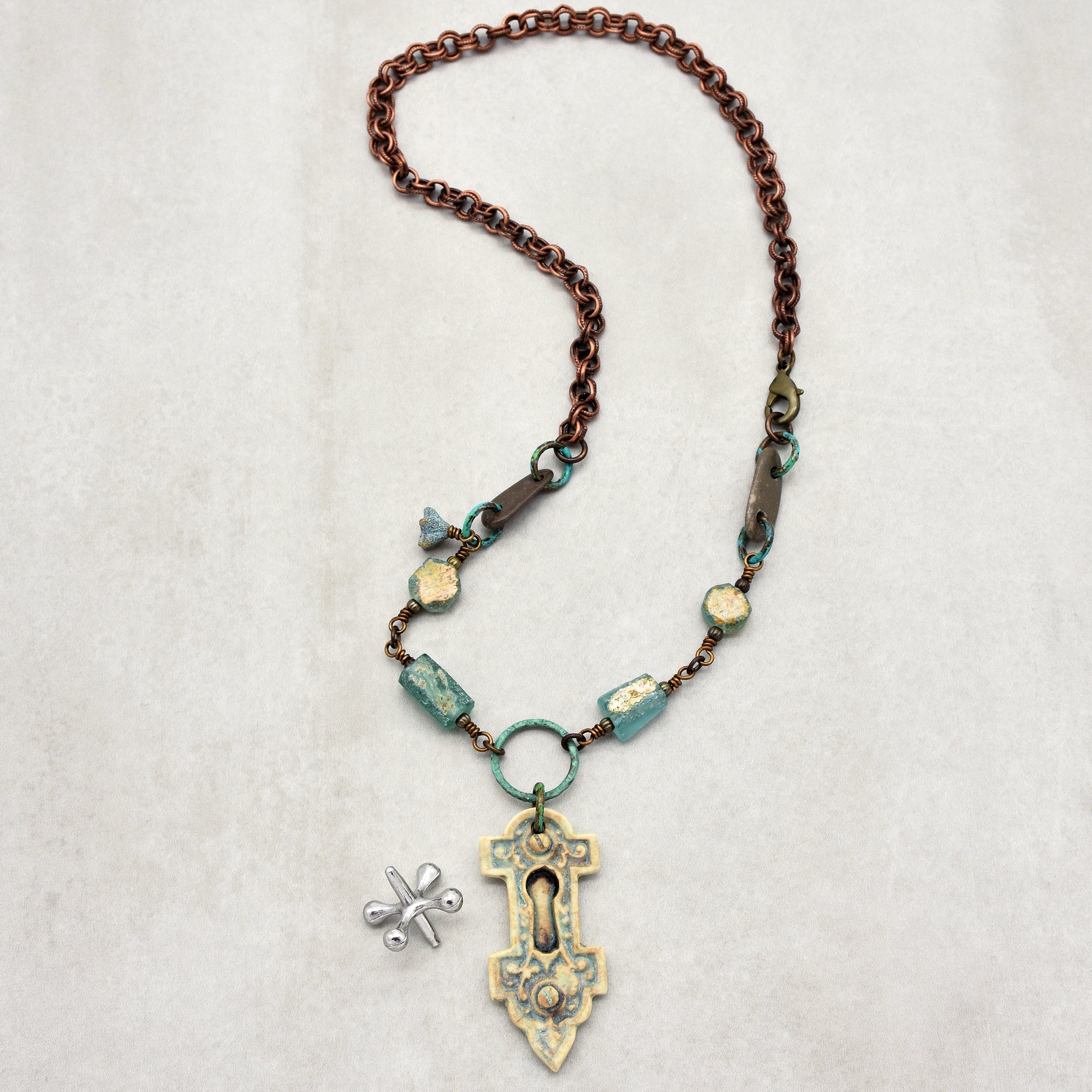 This is a necklace. It features a chain with decorative beads and a keyhole-shaped pendant hanging at the center. There is also a small silver dragonfly charm next to it.