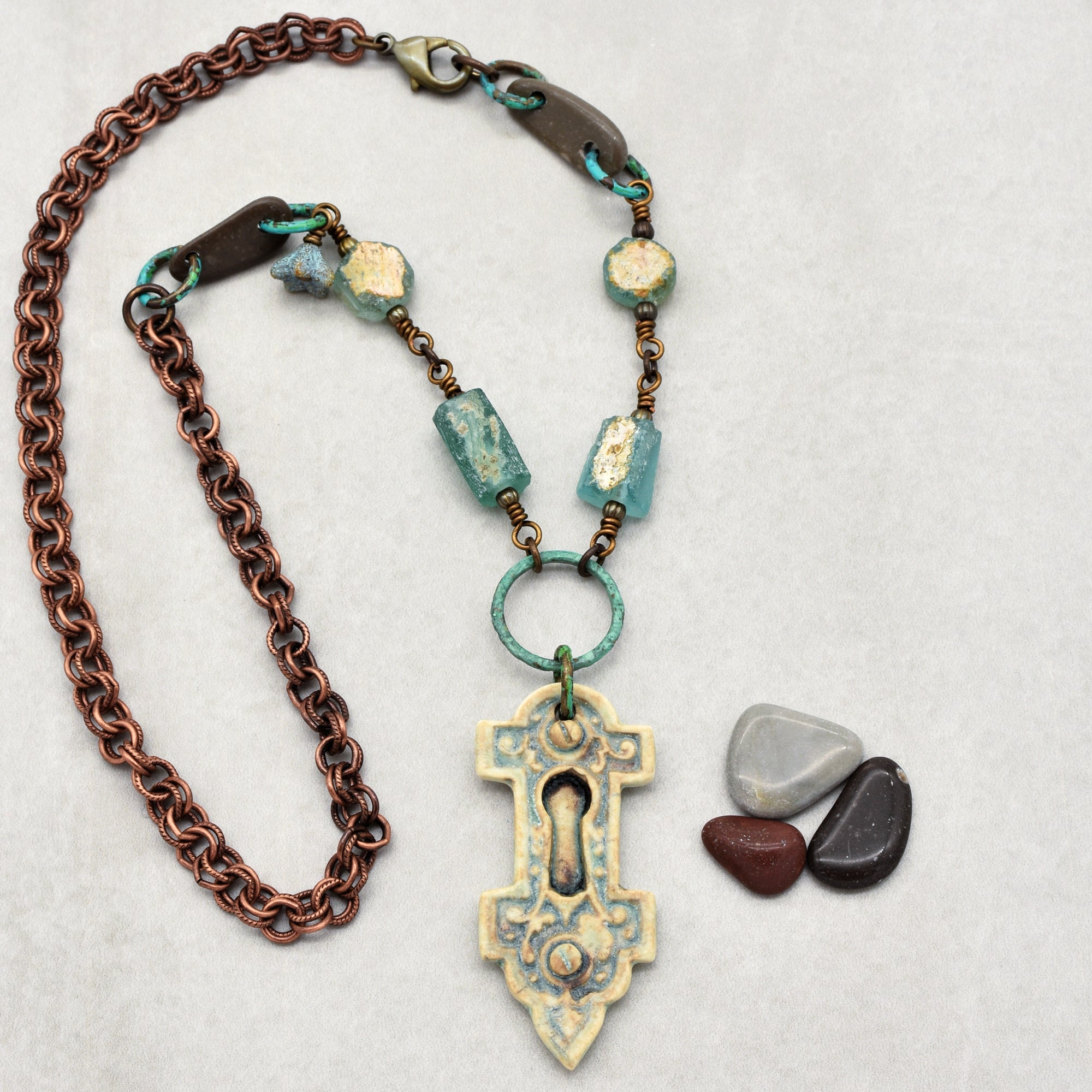 This image shows a necklace. The jewelry features a chain with a decorative pendant that resembles an antique keyhole plate, along with turquoise and brown beads integrated into the design.