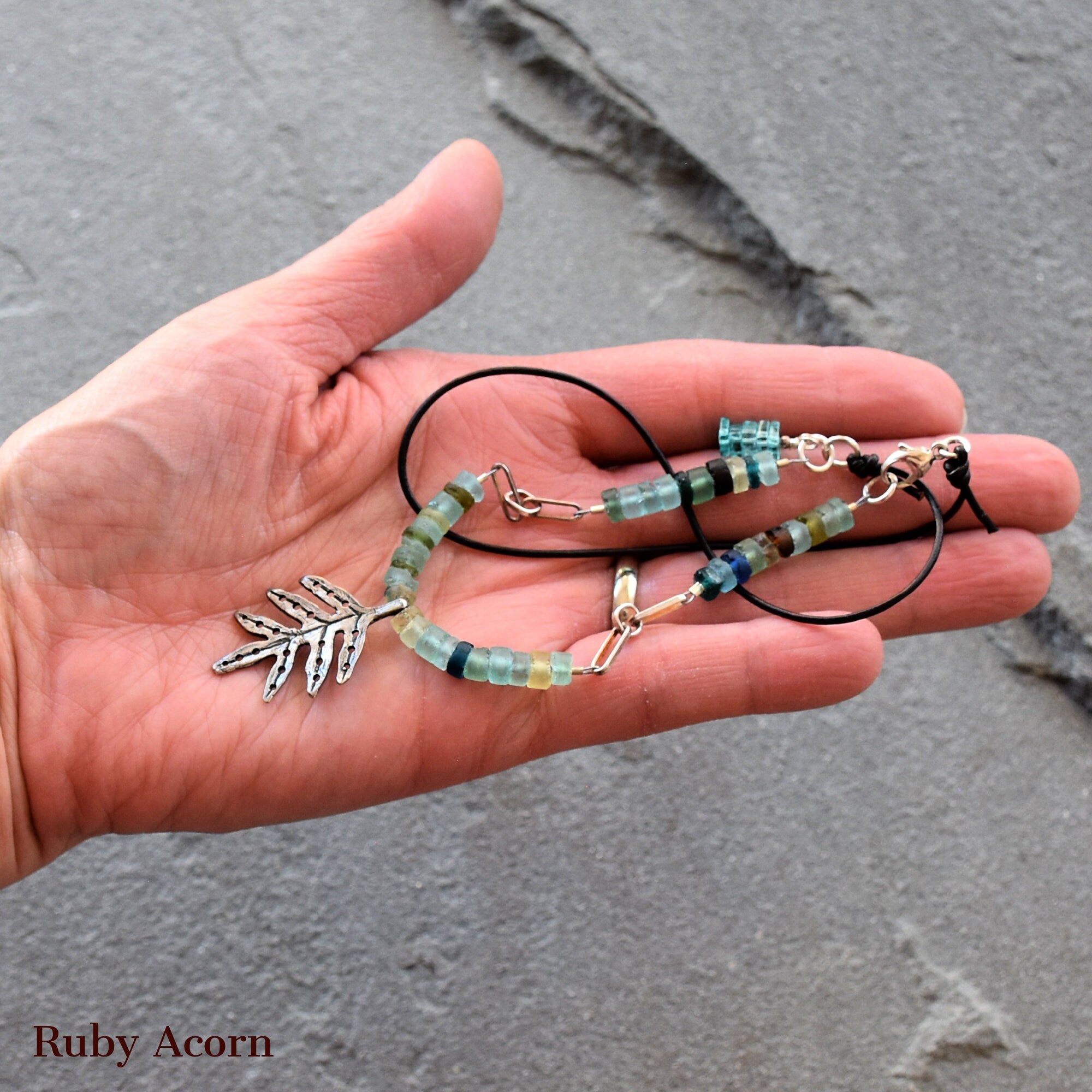 This image shows a bracelet. It features beads and a leaf-shaped charm on a string or cord, which is typical of bracelet designs.