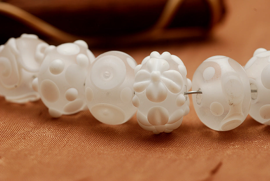 White lampwork glass rondelle beads by Grace Ma with raised floral and dot details and a frosted matte finish.