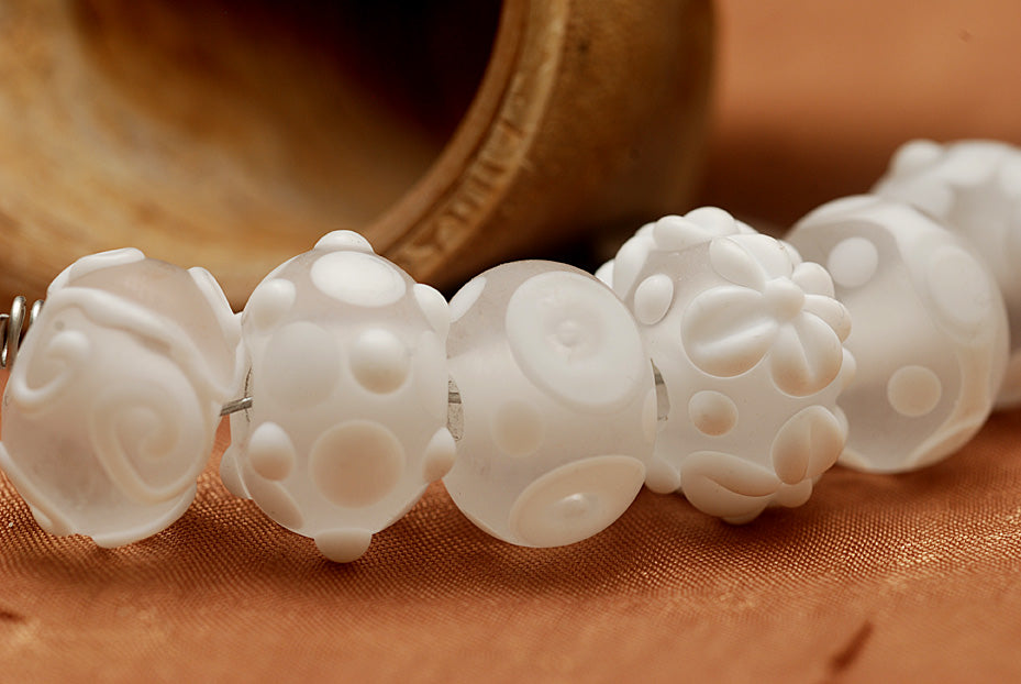 White lampwork glass rondelle beads by Grace Ma with raised floral and dot details and a frosted matte finish.