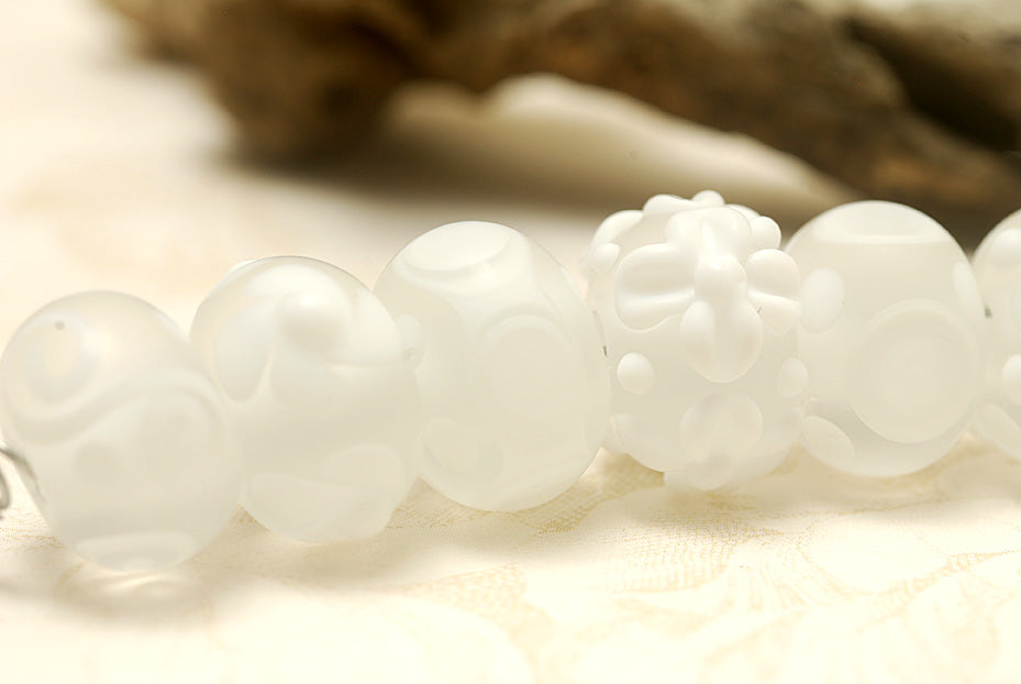 White lampwork glass rondelle beads by Grace Ma with raised floral and dot details and a frosted matte finish.
