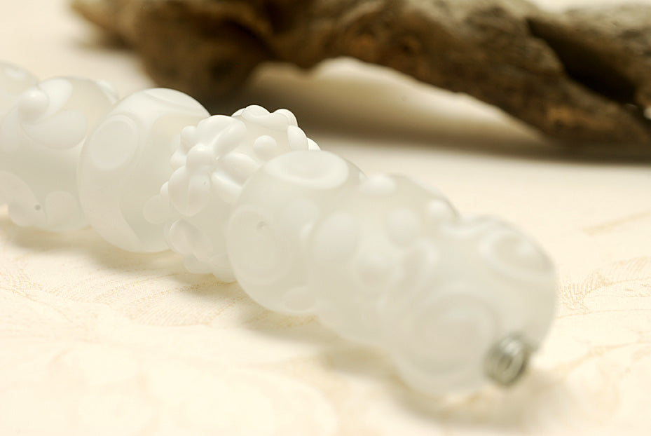 White lampwork glass rondelle beads by Grace Ma with raised floral and dot details and a frosted matte finish.