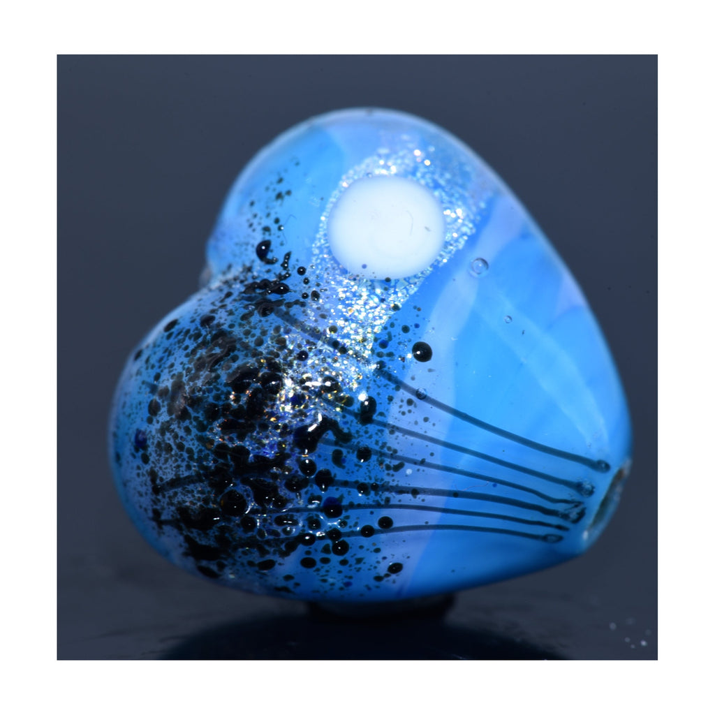 Blue heart-shaped pendant with black speckles on a dark background - Grace Lampwork Beads available at Ruby Acorn.