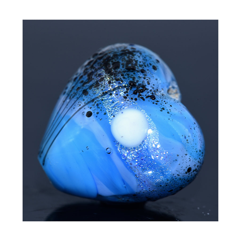 Blue heart-shaped pendant with black speckles on a dark background - Grace Lampwork Beads available at Ruby Acorn.