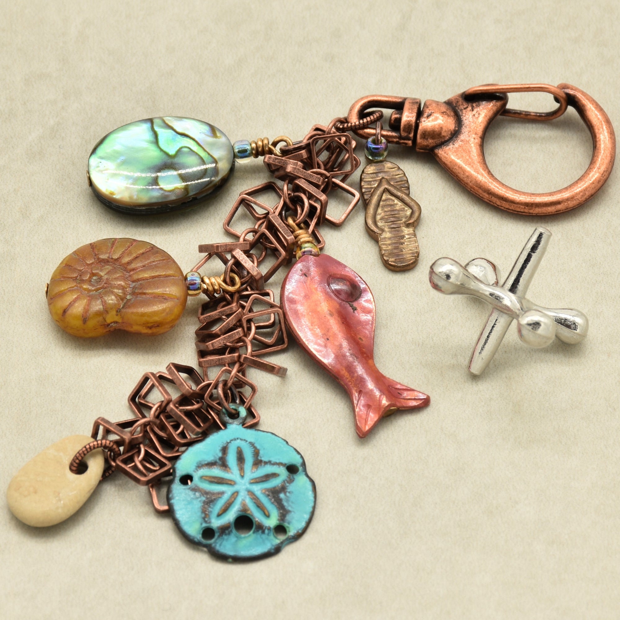 Keychain with various charms including a fish, sand dollar, ammonite, and abalone on a beige background