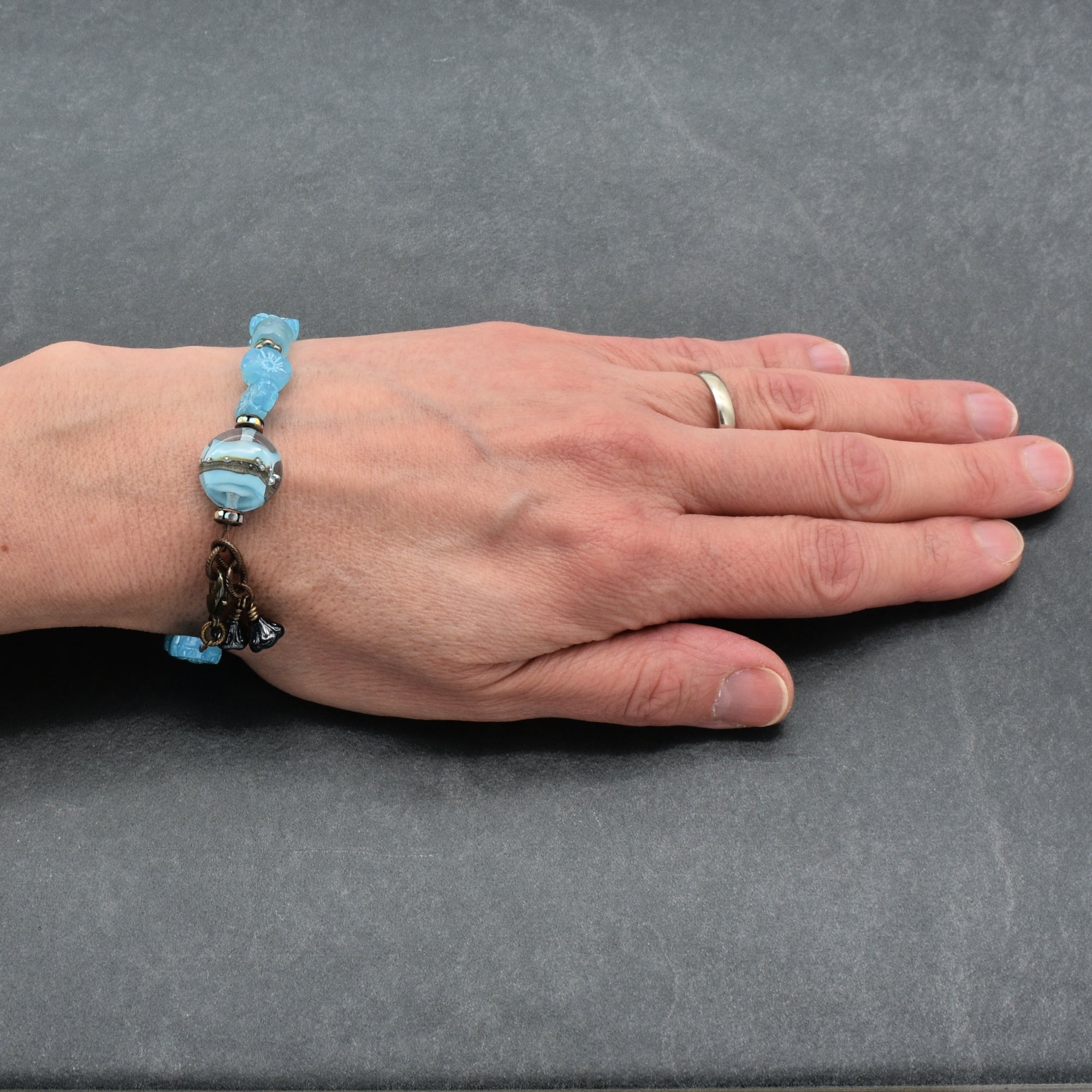 Hand wearing a bracelet with blue beads on a gray background