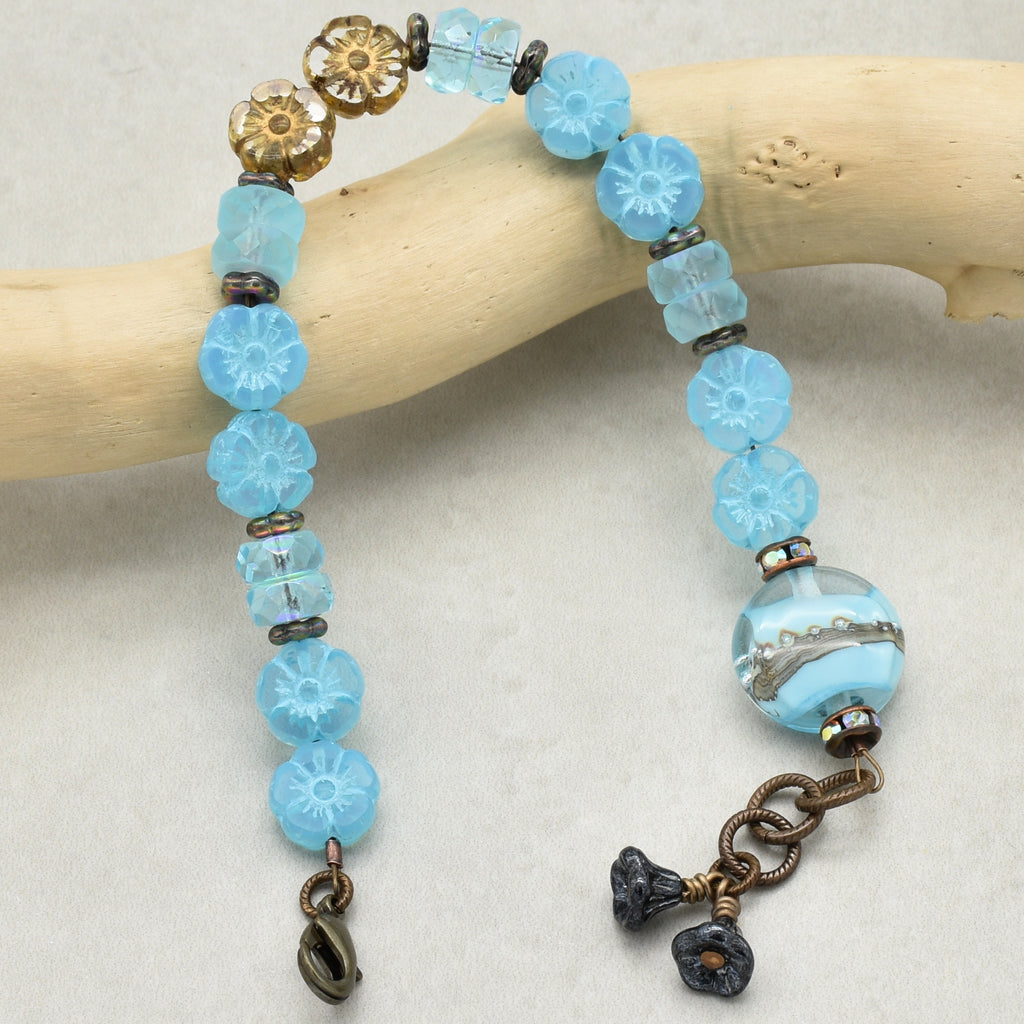 Blue beaded bracelet with floral charms on a wooden stick against a white background