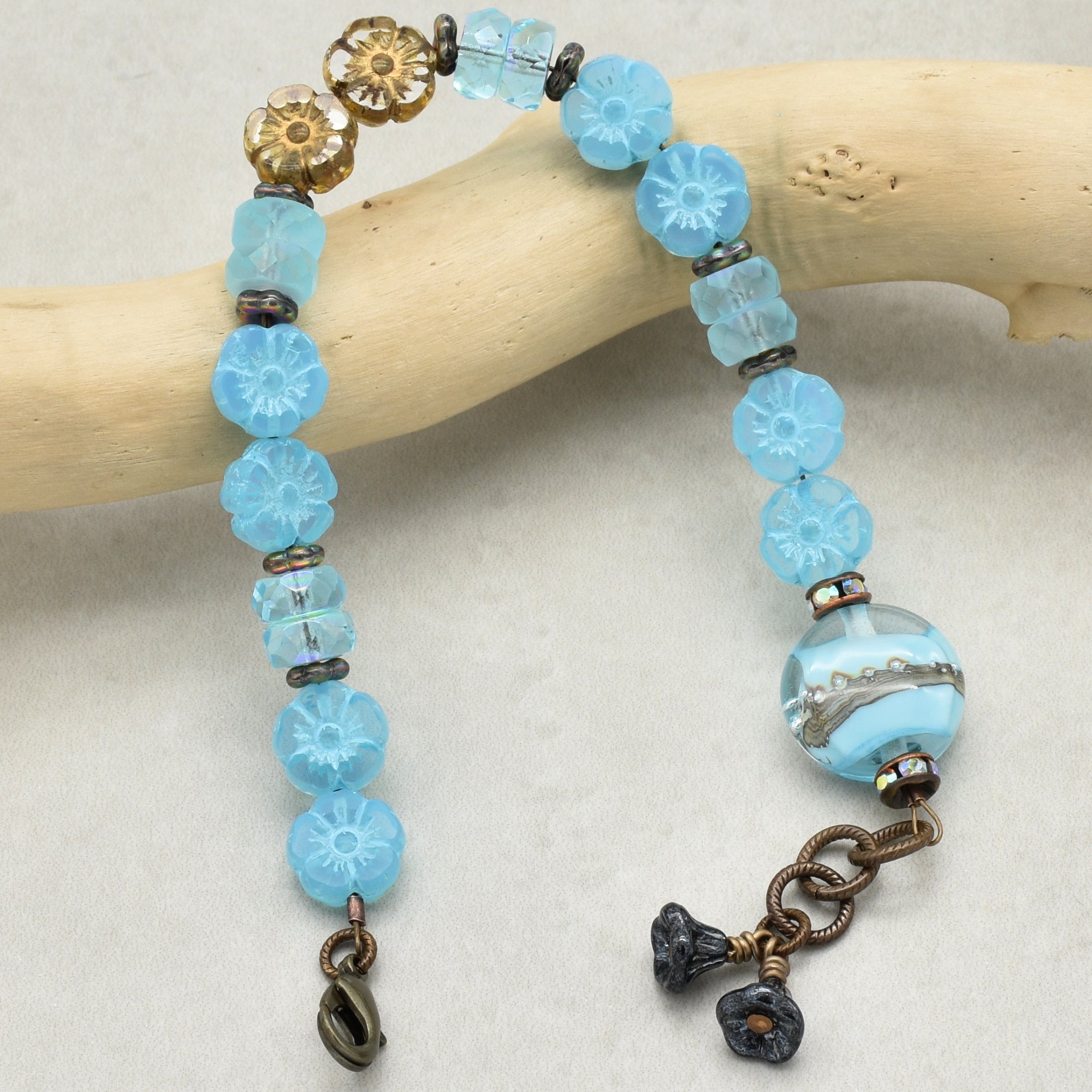 Blue beaded bracelet with floral charms on a wooden stick against a white background