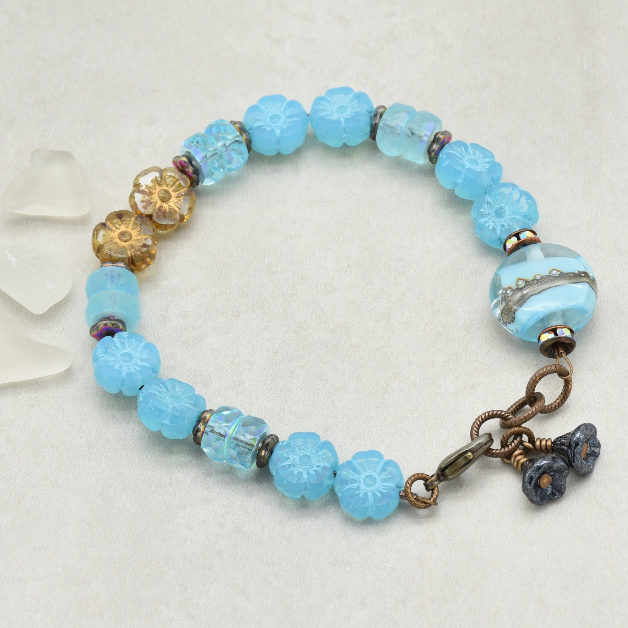 Blue beaded bracelet with floral charm on a light gray background