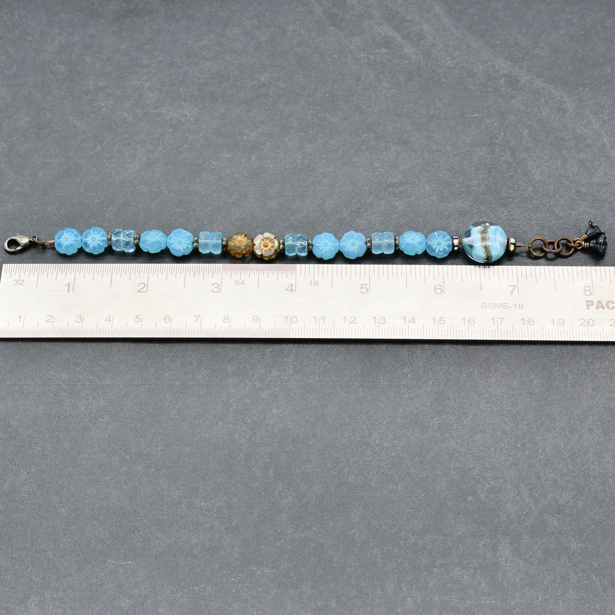 Beaded bracelet with blue and gold beads on a gray surface with a ruler for scale.