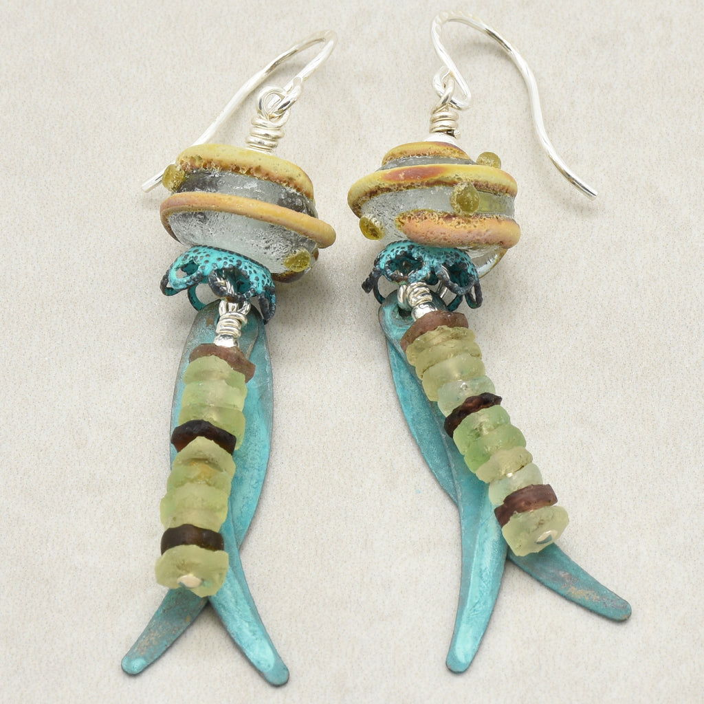 A pair of handmade dangle earrings featuring ancient Roman glass, artisan lampwork glass, verdigris daggers,  silver ear wires, displayed on a neutral background - made with love in Colorado by Ruby Acorn.