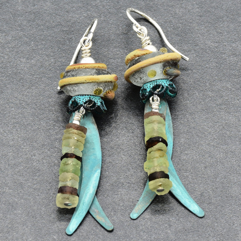 A pair of handmade dangle earrings featuring ancient Roman glass, artisan lampwork glass, verdigris daggers,  silver ear wires, displayed on a dark gray textured background - made with love in Colorado by Ruby Acorn.
