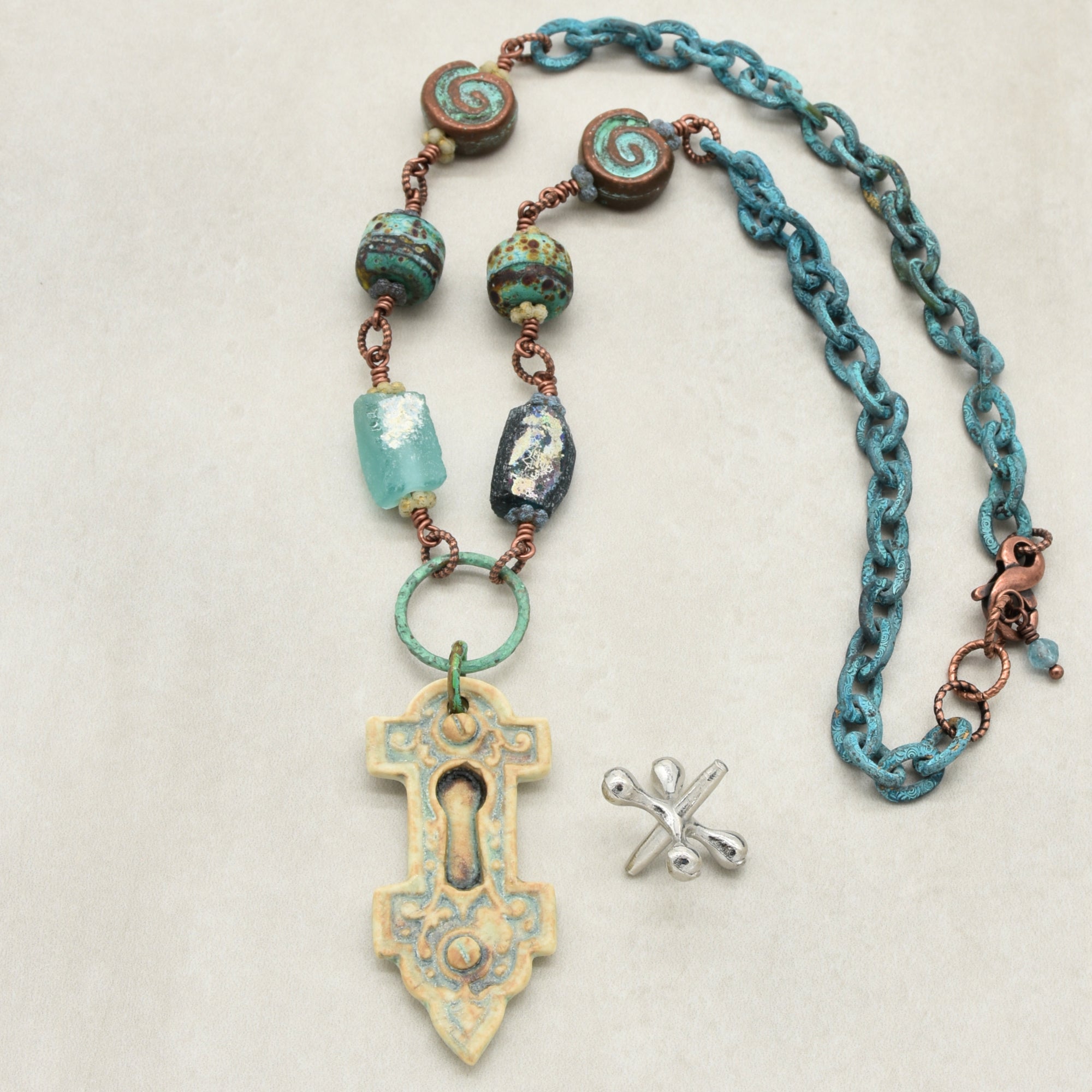 A handmade necklace with an artisan porcelain keyhole pendant, ancient Roman glass beads, and verdigris chain, displayed on a light beige background - made with love in Colorado by Ruby Acorn.
